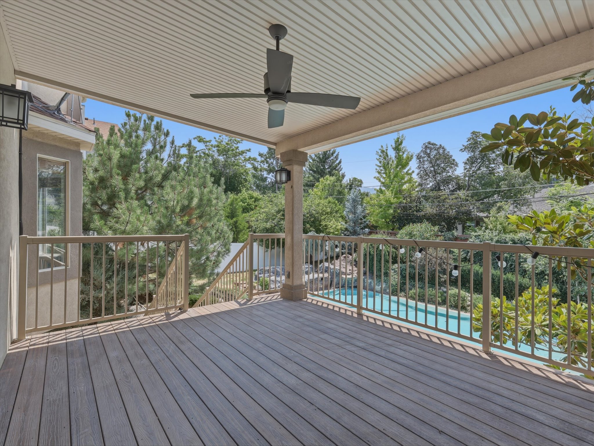 Spacious covered deck featuring wood-finish composite decking, a ceiling fan, recessed lighting, and a balustrade overlooking a swimming pool