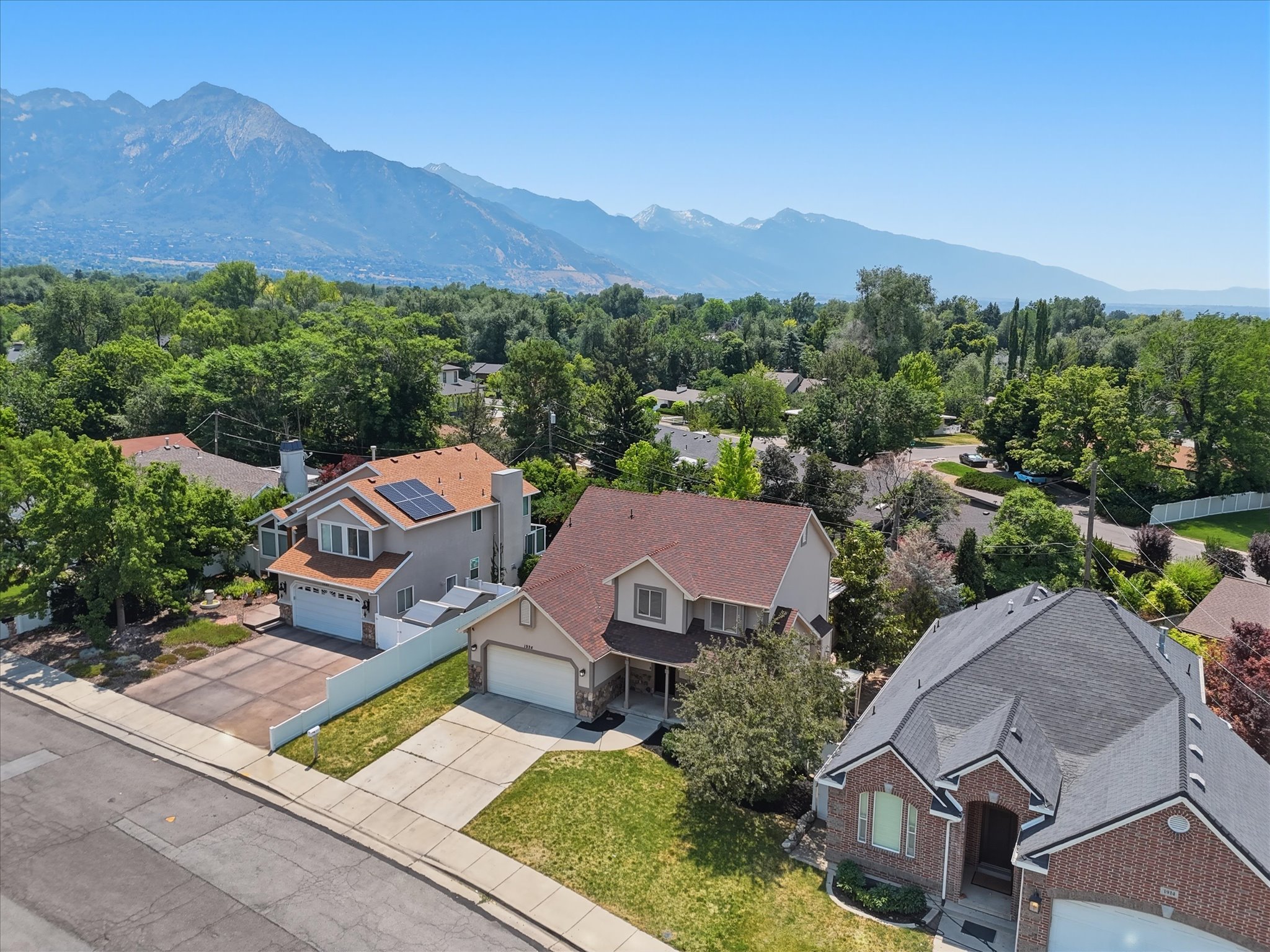 Neighborhood street with established properties and mature landscaping framed by distant mountains