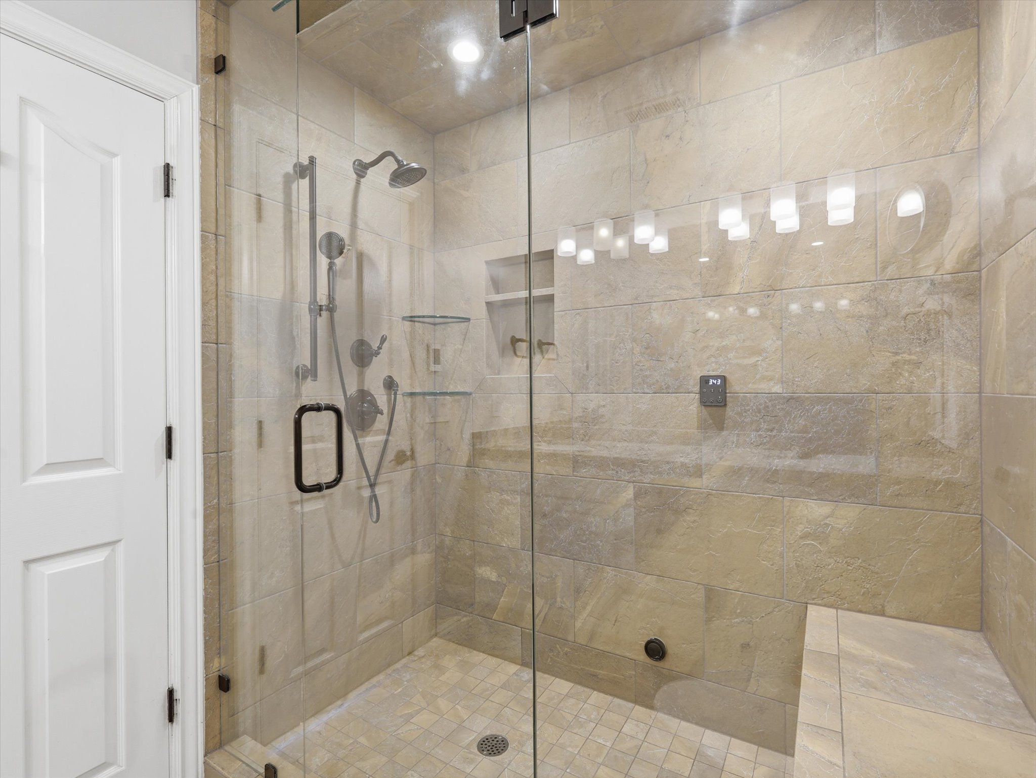 Spacious shower enclosure featuring full-height tile walls, a built-in bench, and a frameless glass door