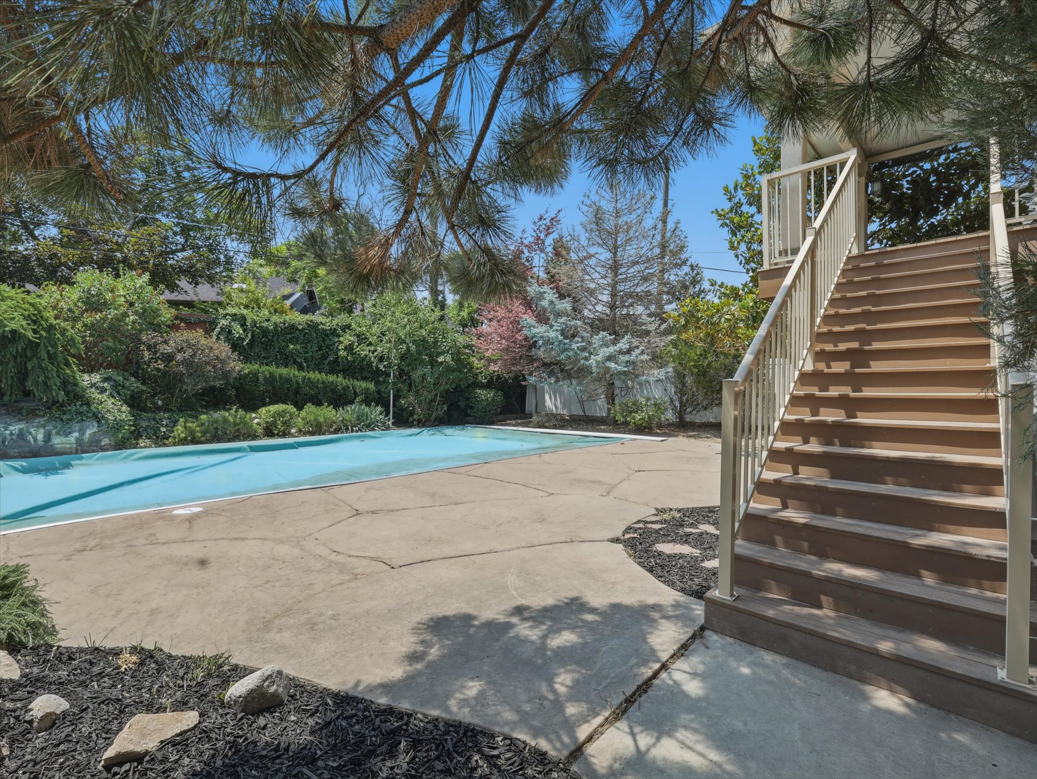 Outdoor pool area featuring a covered swimming pool, concrete patio, and mature landscaping