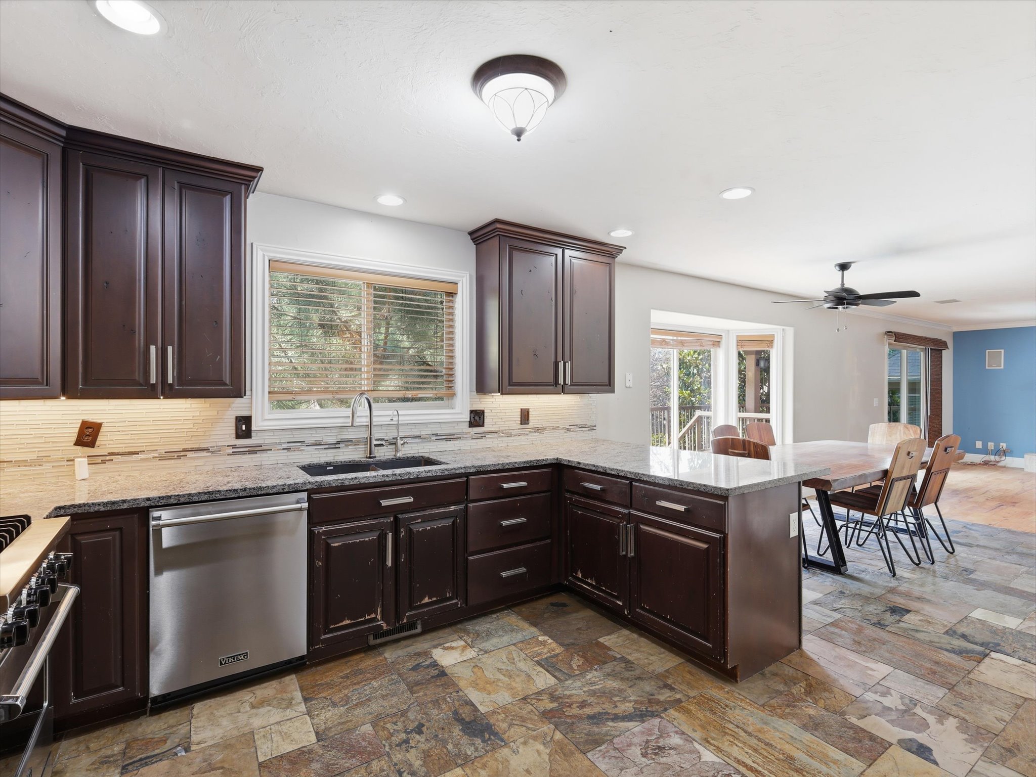 Kitchen featuring dark wood cabinetry, light-toned countertops, a stainless steel dishwasher, and a tile backsplash