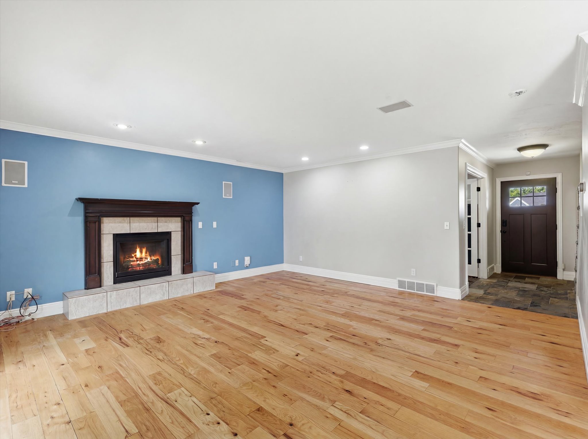 Spacious interior featuring wood-finish flooring, a fireplace with a stone surround and dark wood mantel, recessed lighting, and crown molding