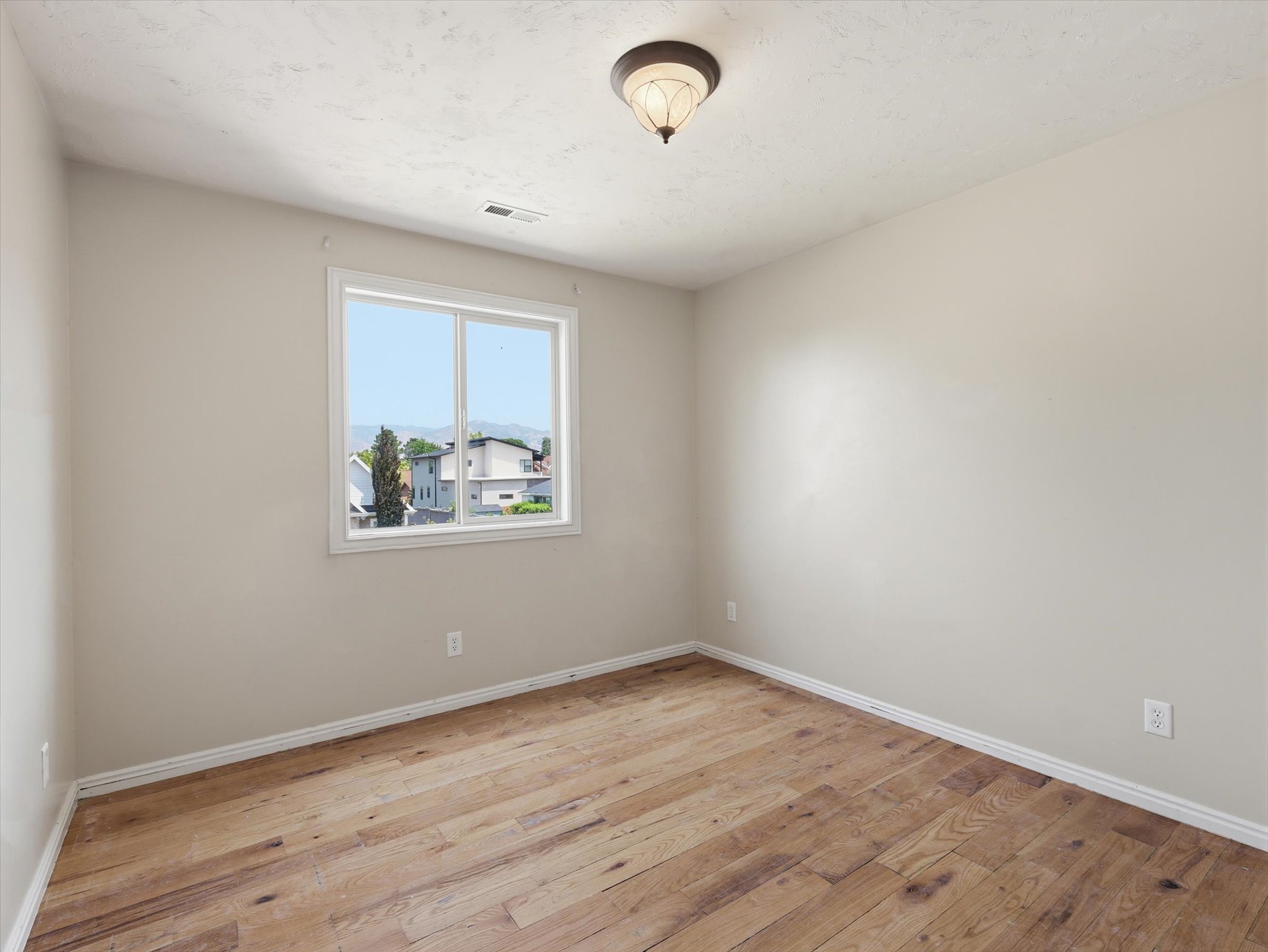 Room featuring wood-finish flooring, a white trim baseboard, and a double-pane window