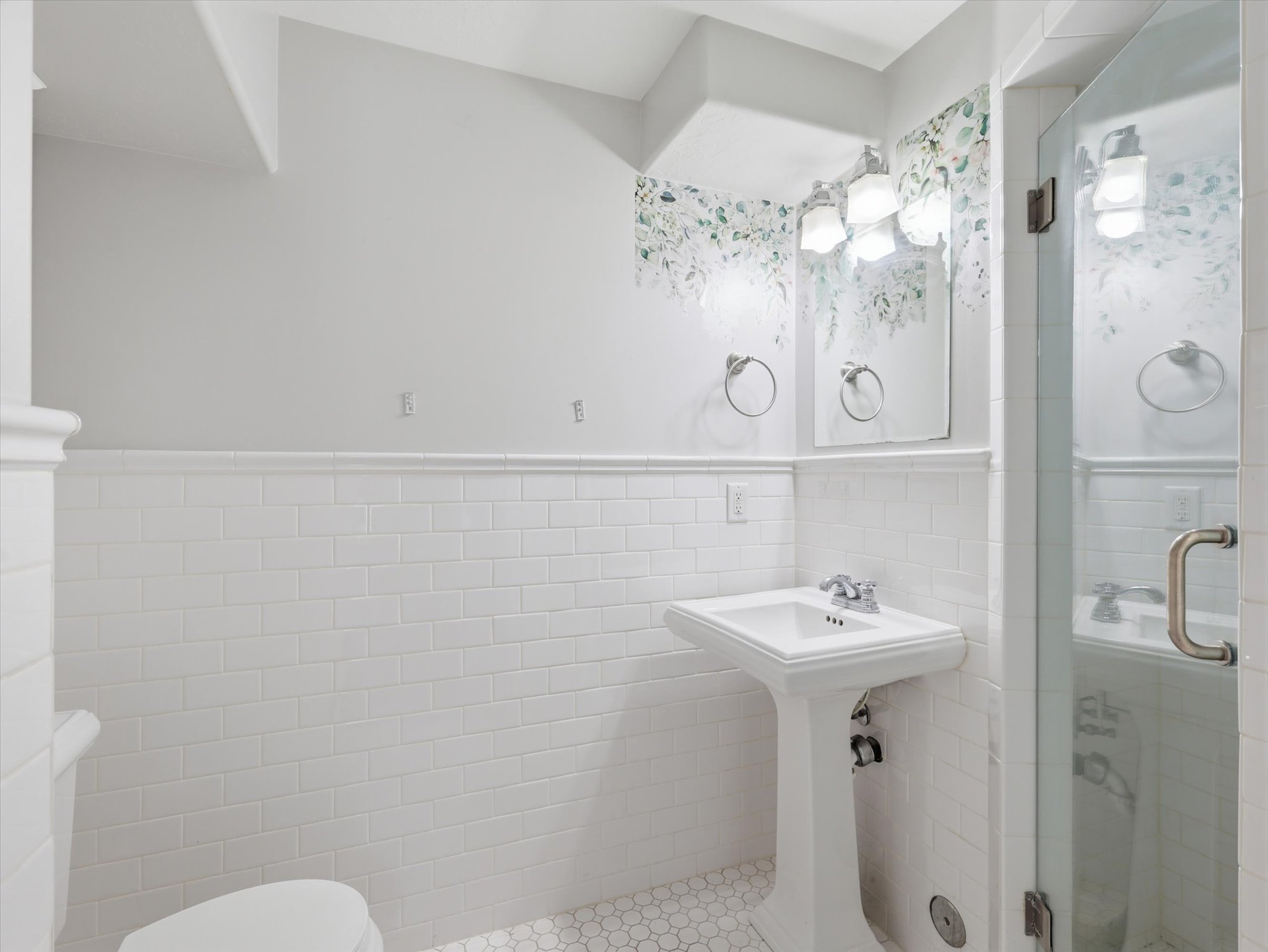Bathroom featuring a glass-enclosed shower, pedestal sink, chrome fixtures, and white subway tile wainscoting