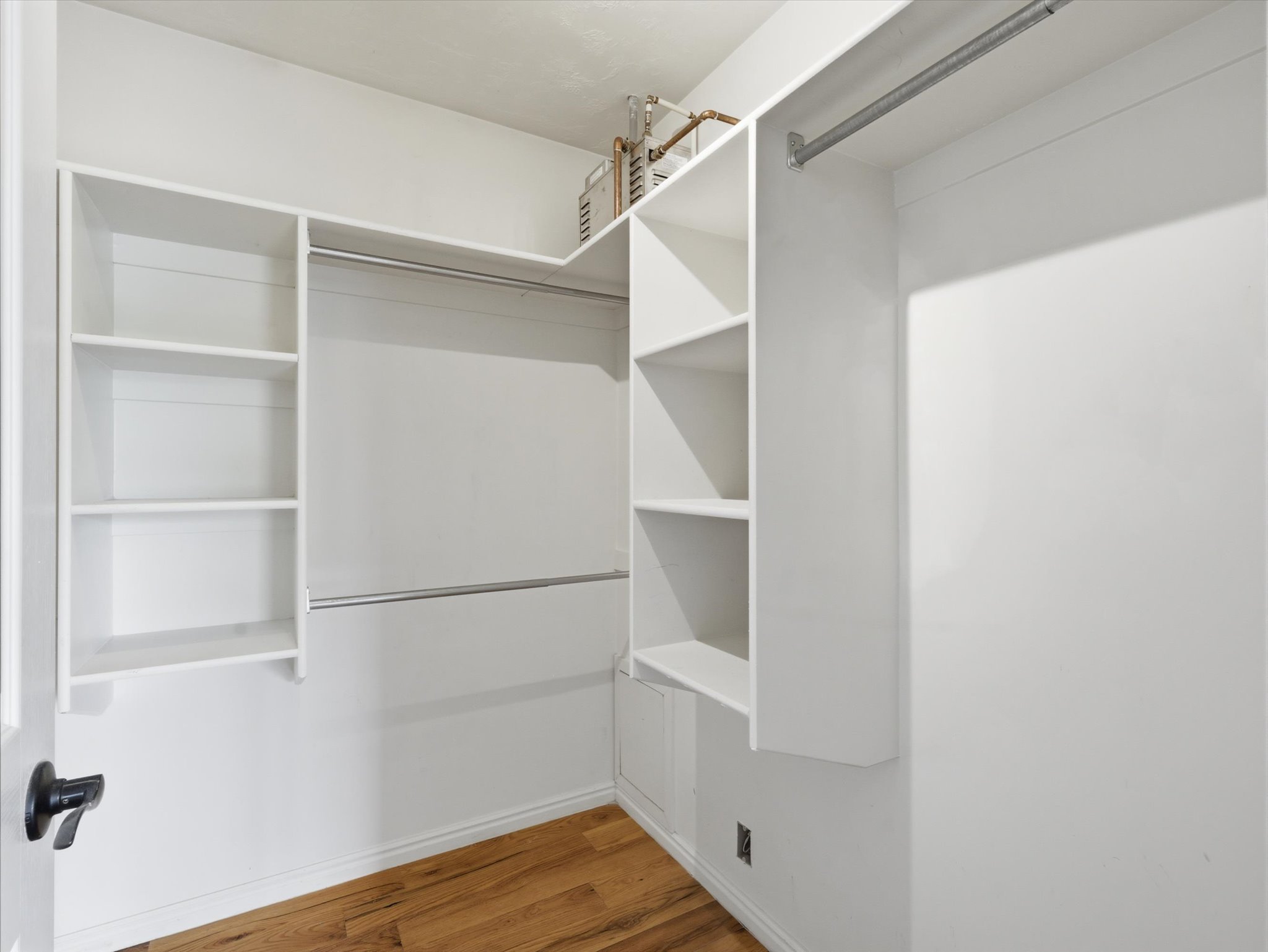 Walk-in closet featuring white built-in shelving, multiple hanging rods, and wood-finish flooring