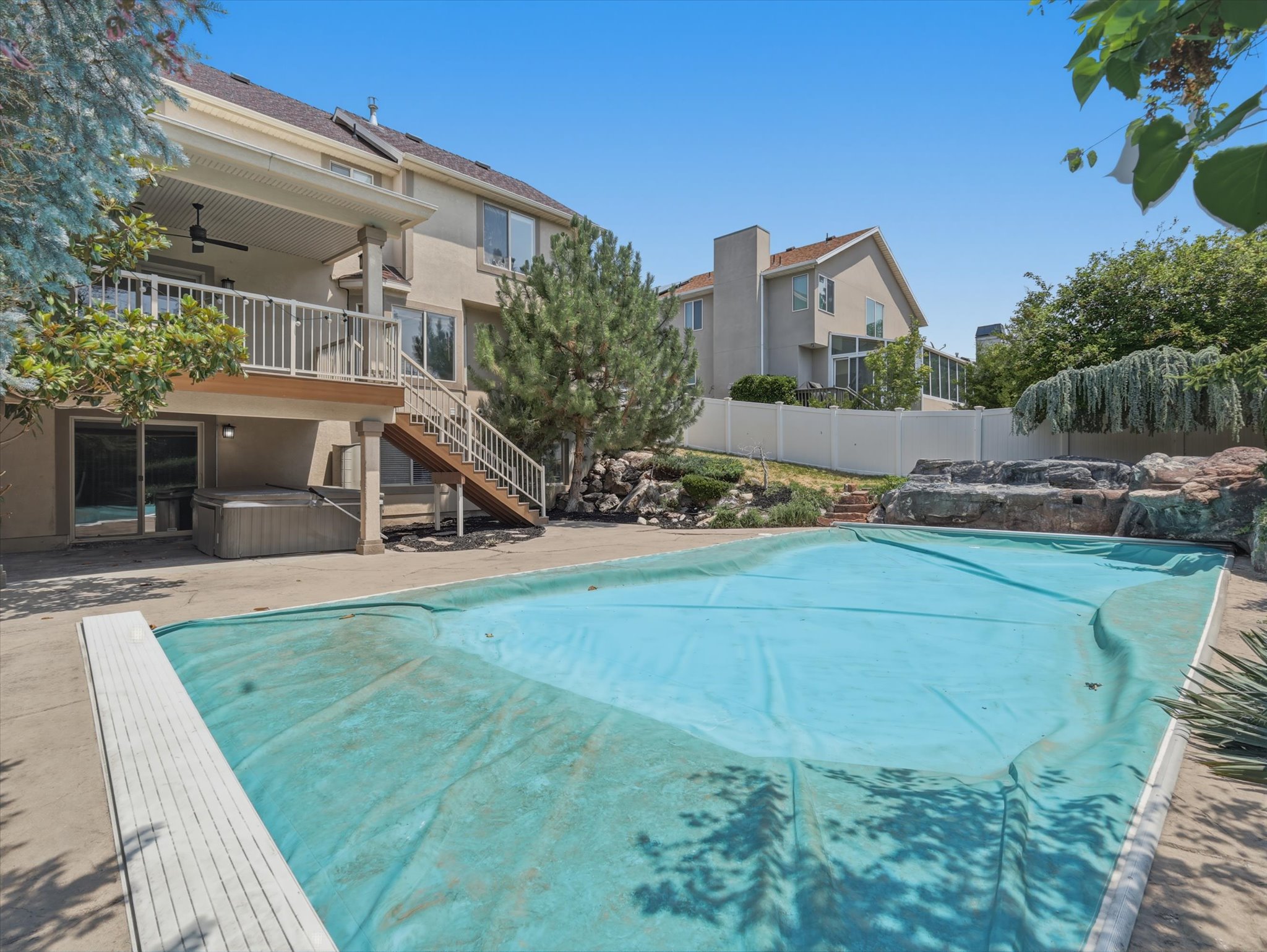 Covered swimming pool with rock waterfall feature, concrete pool deck, and a lower-level hot tub