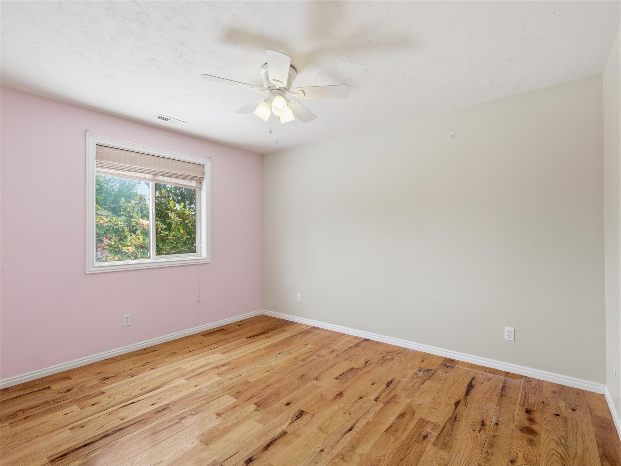 Light-filled room featuring wood-finish flooring, a window with exterior greenery, and a ceiling fan with integrated lighting