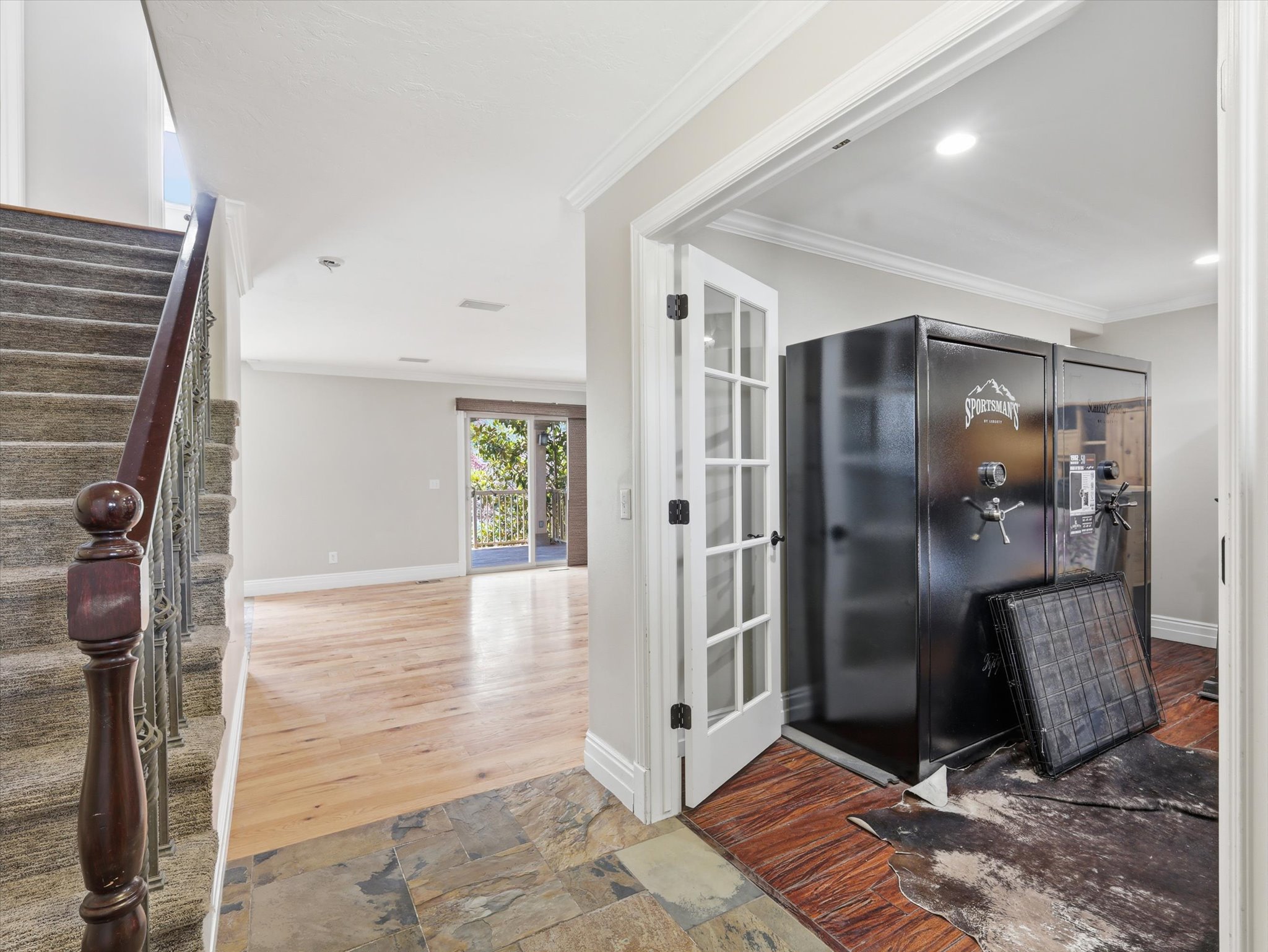 Entryway featuring slate tile flooring, wood-finish flooring, a carpeted staircase with a dark wood handrail and wrought iron balusters, and crown molding
