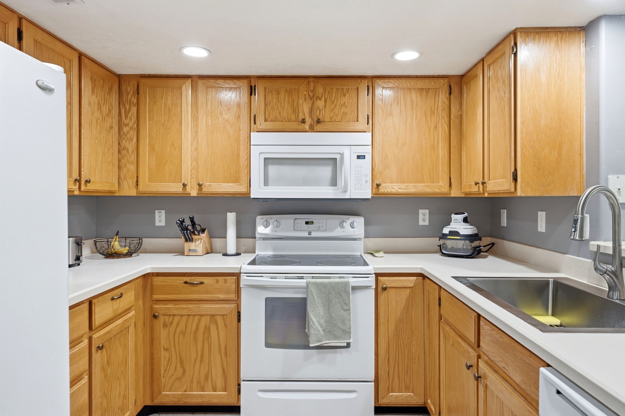U-shaped kitchen featuring wood-finish cabinetry, white countertops, a double basin stainless steel sink, and recessed lighting