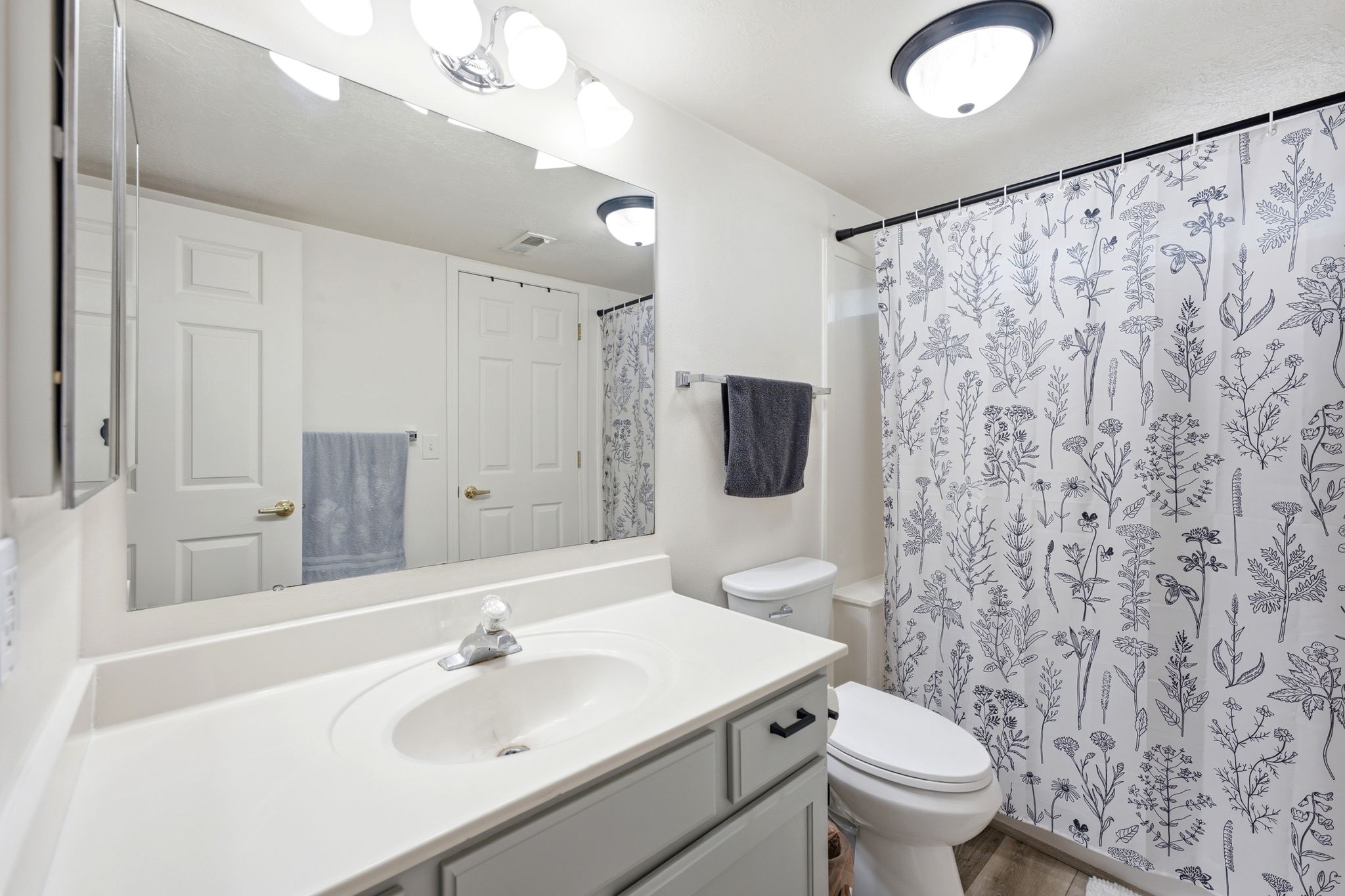 Bathroom vanity featuring a single basin sink, light-toned countertop, and light gray cabinetry with dark hardware
