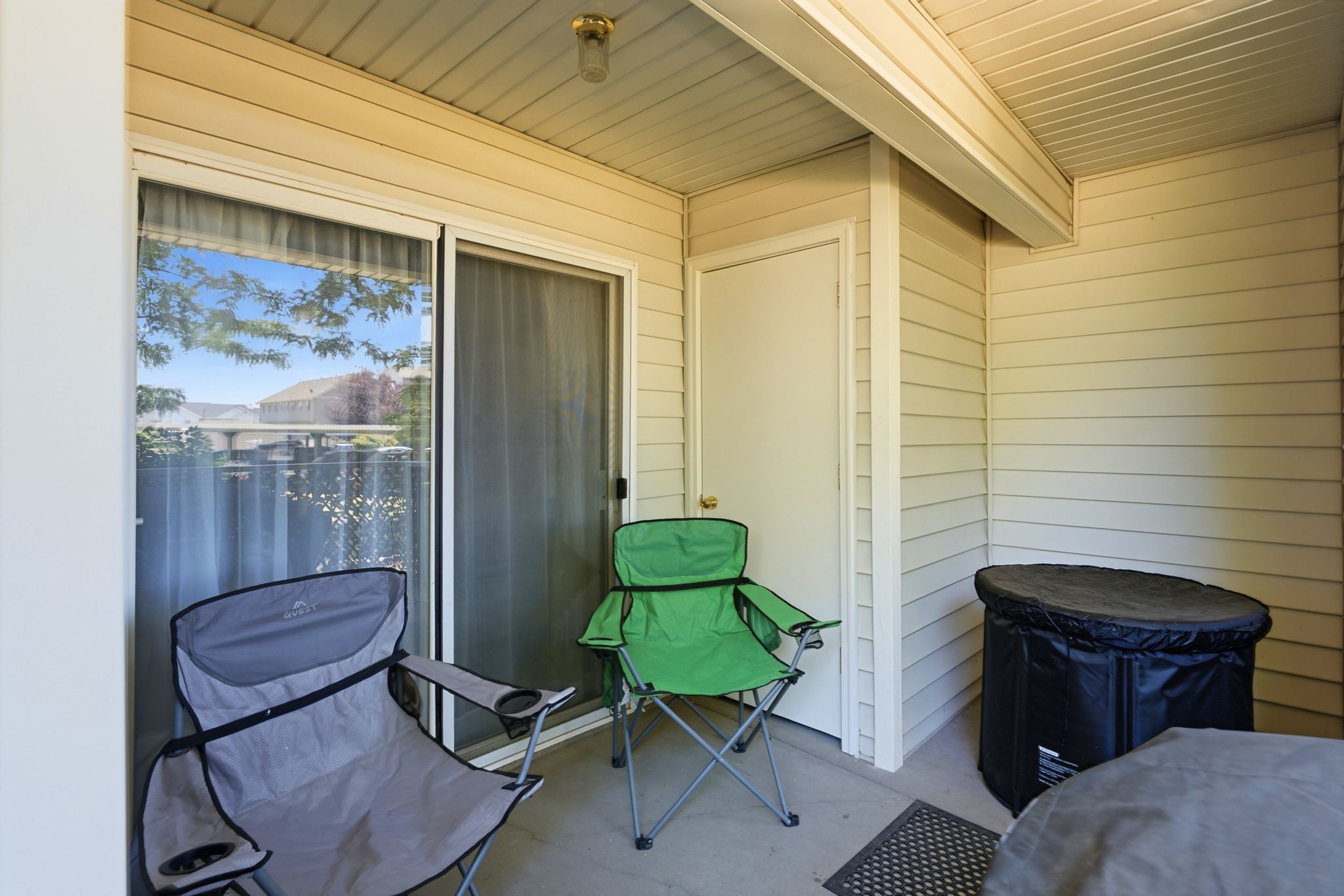 Covered outdoor patio featuring beige siding, concrete flooring, and an exterior storage door