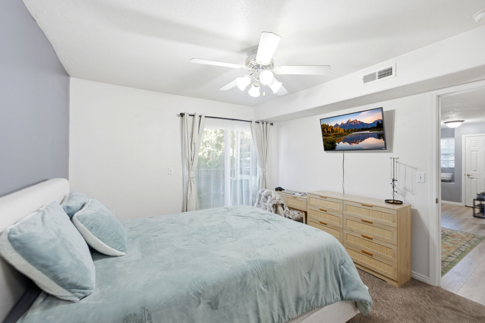 Master bedroom featuring a ceiling fan, light-toned carpeting, and a sliding glass door with sheer and blackout curtains