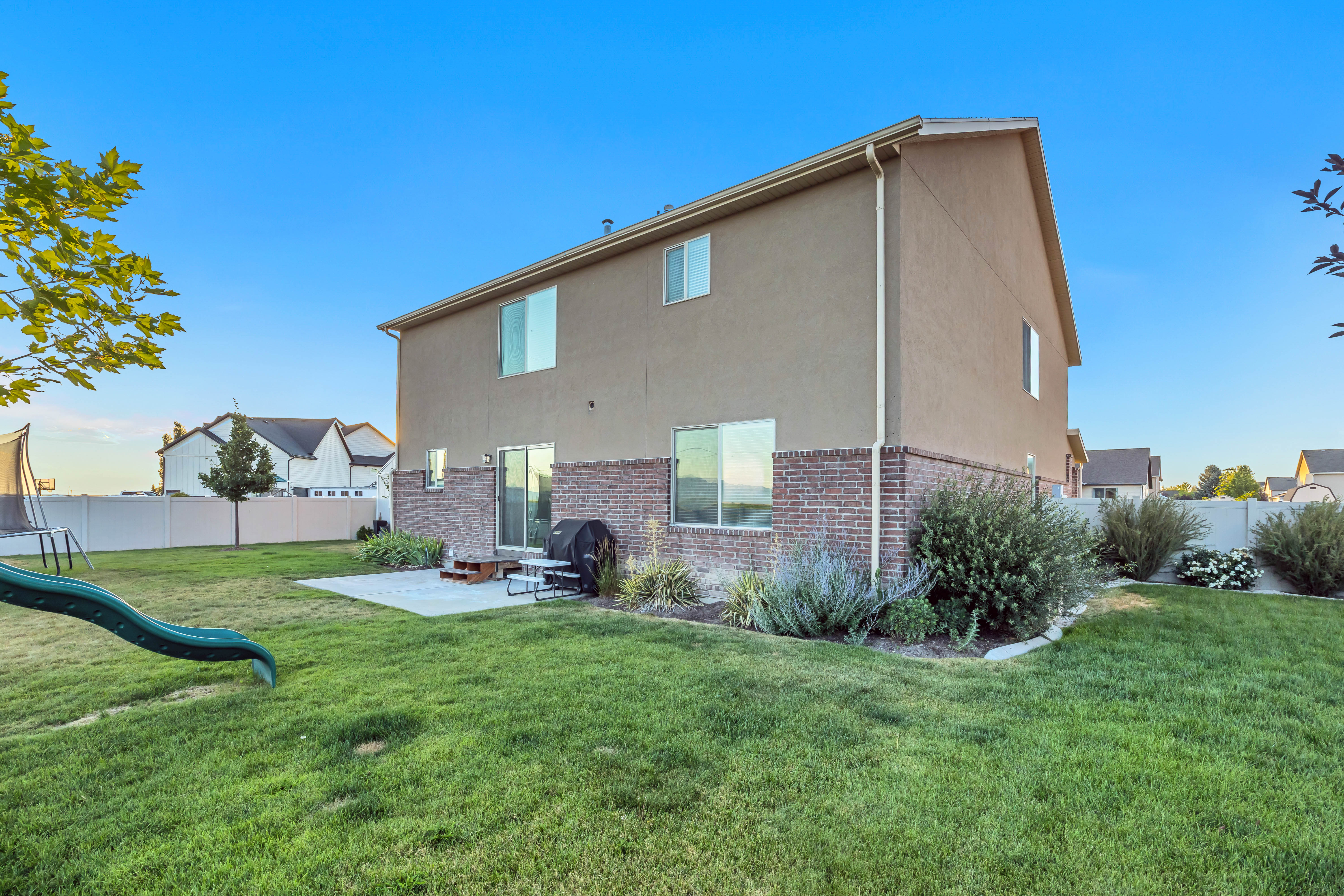 Expansive rear yard featuring a concrete patio, mature shrubs, and a well-maintained lawn