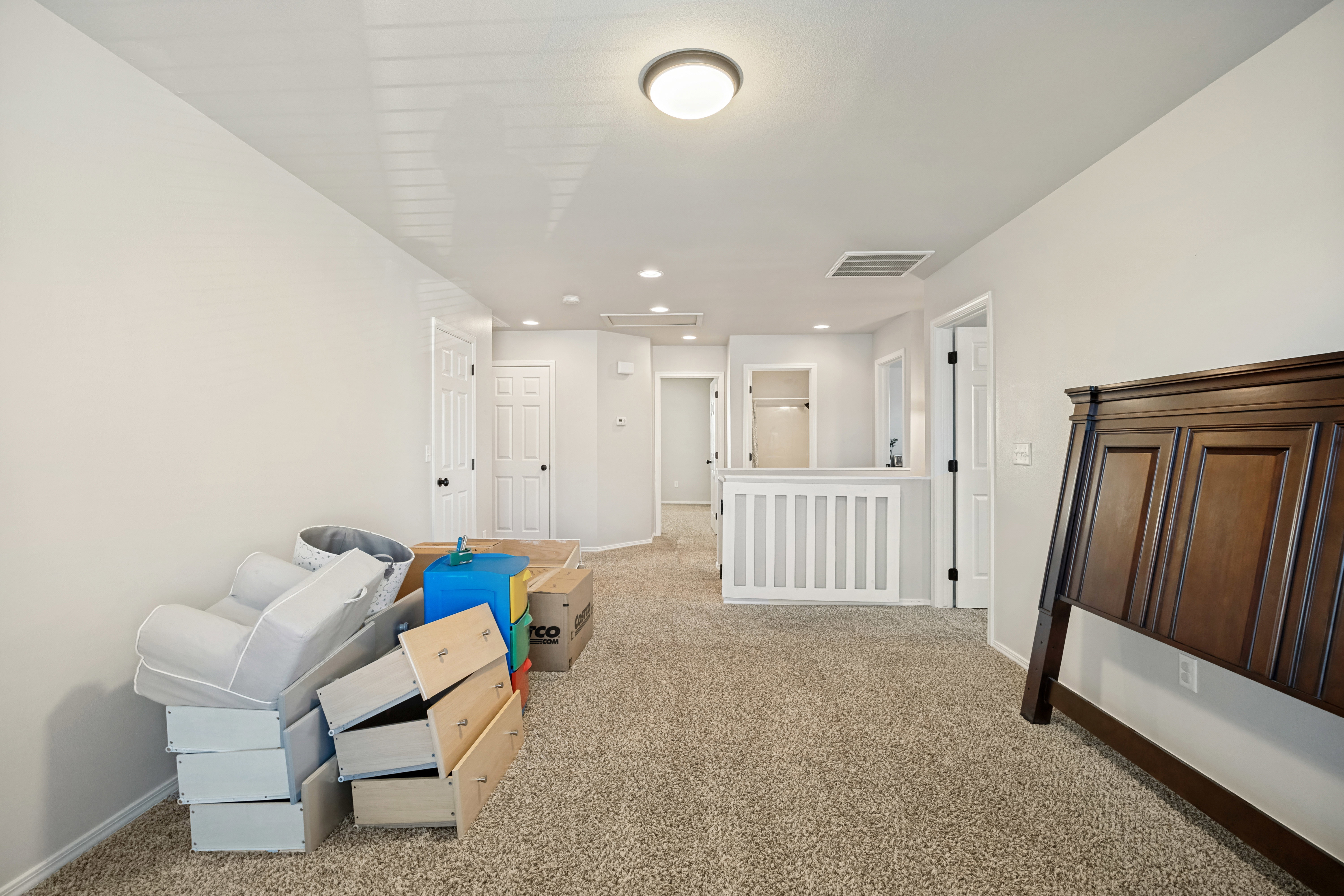 Open concept upper-level area with carpeted flooring, light neutral wall finishes, and a white balustrade overlooking a lower level