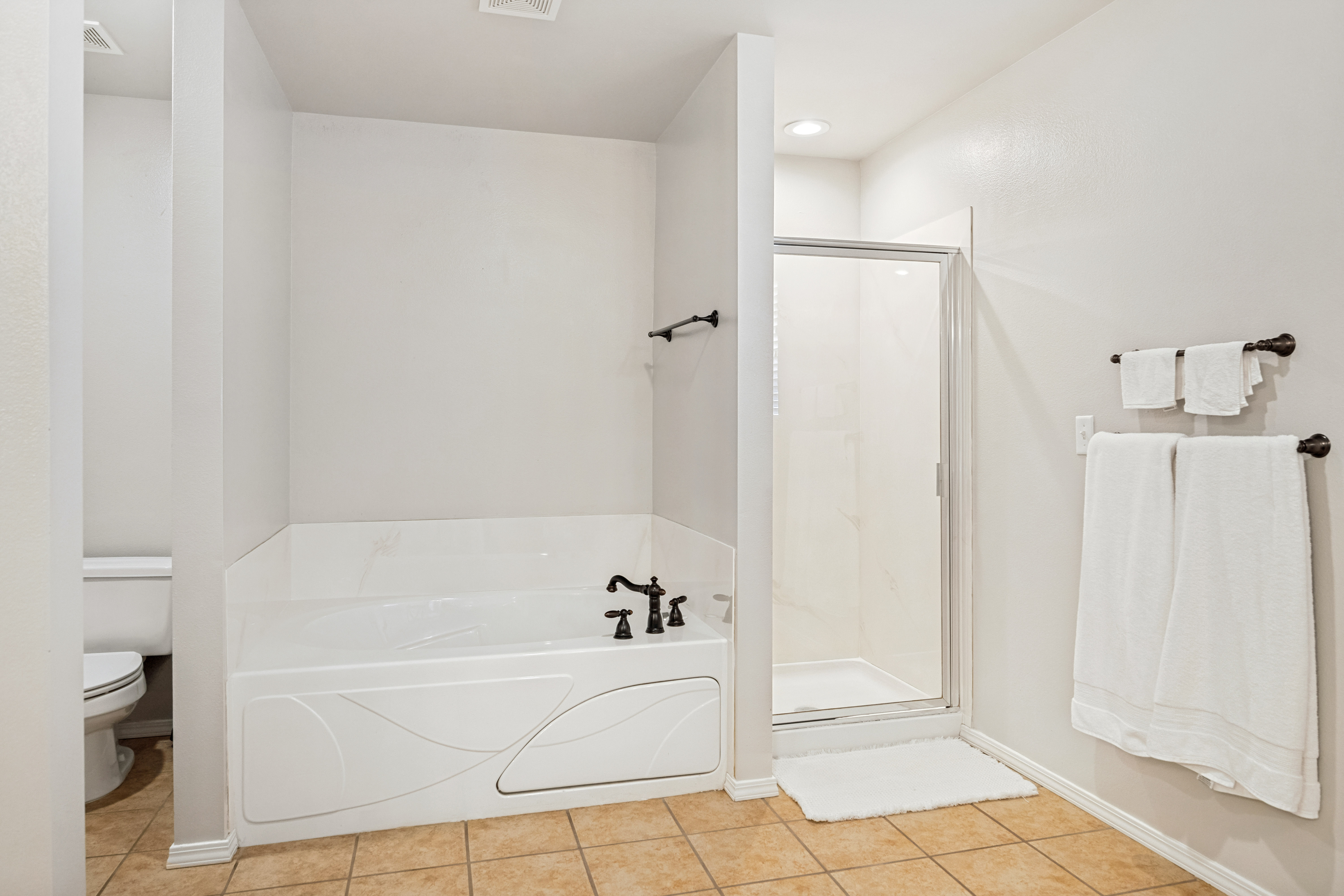 Bathroom featuring a built-in tub with dark bronze fixtures, an enclosed shower with a glass door, and square tile flooring