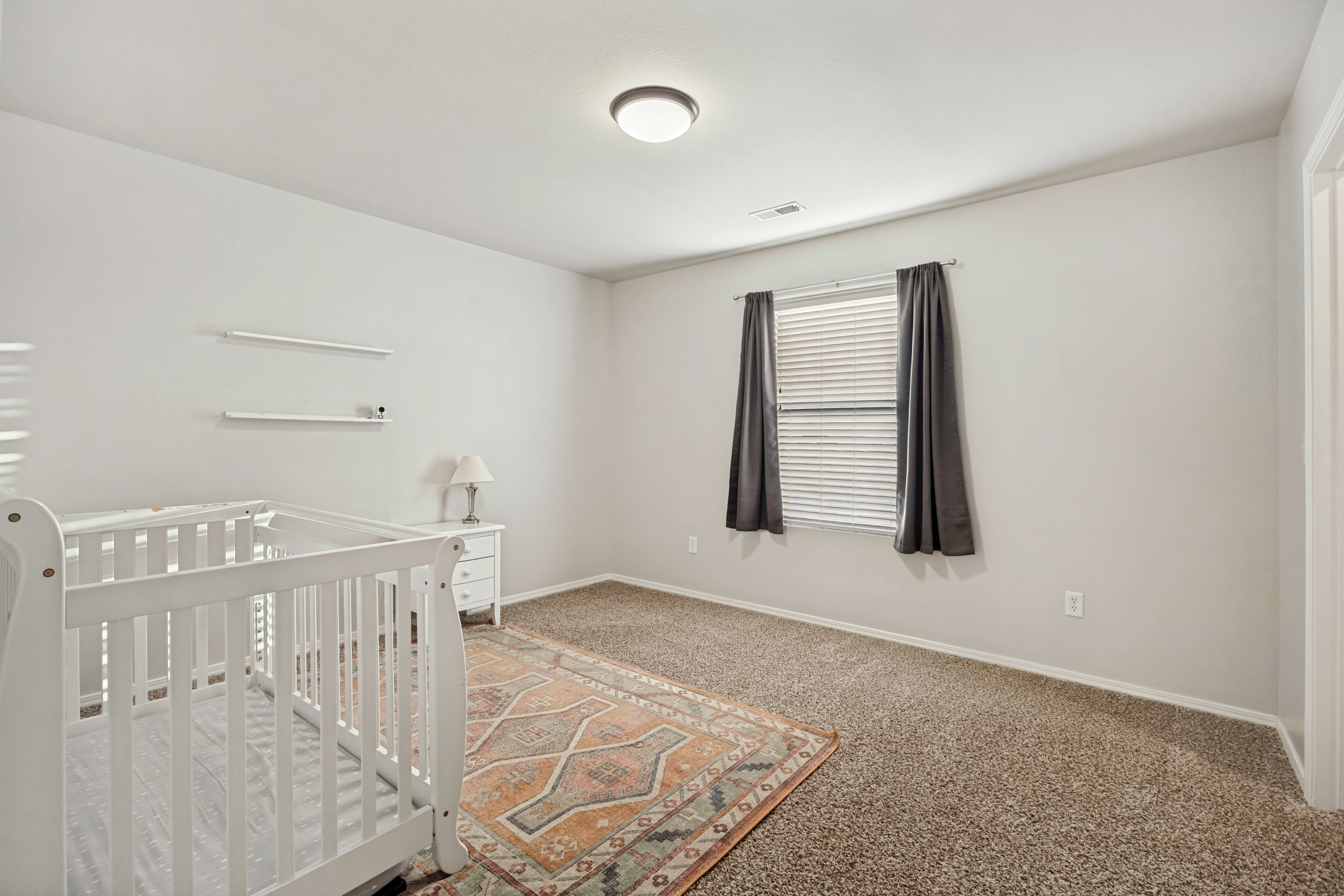 Neutral wall paint with carpeted flooring, featuring a window with blinds and dark-toned curtains