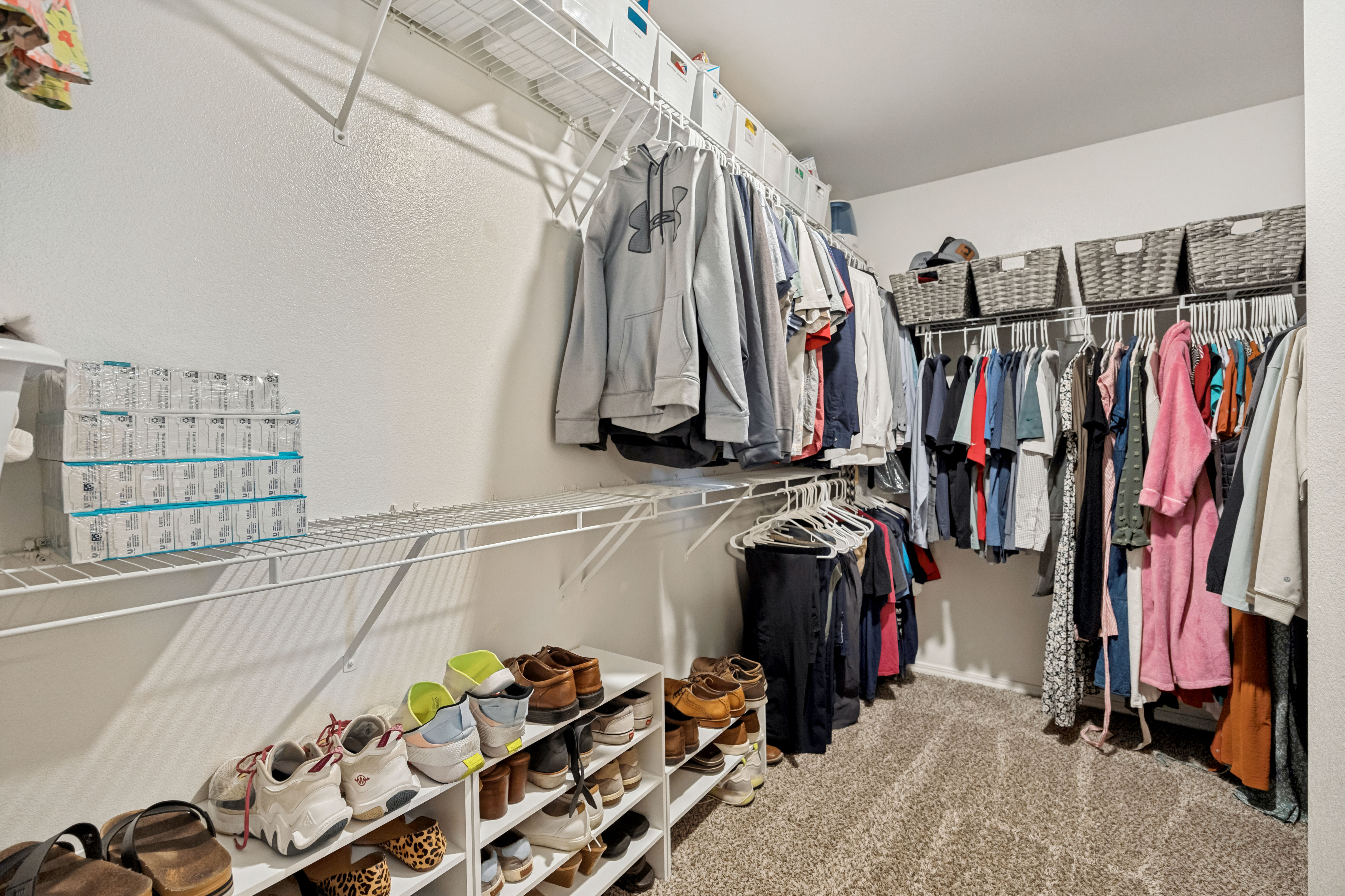Spacious closet featuring white wire shelving, multiple hanging rods, and neutral carpet flooring