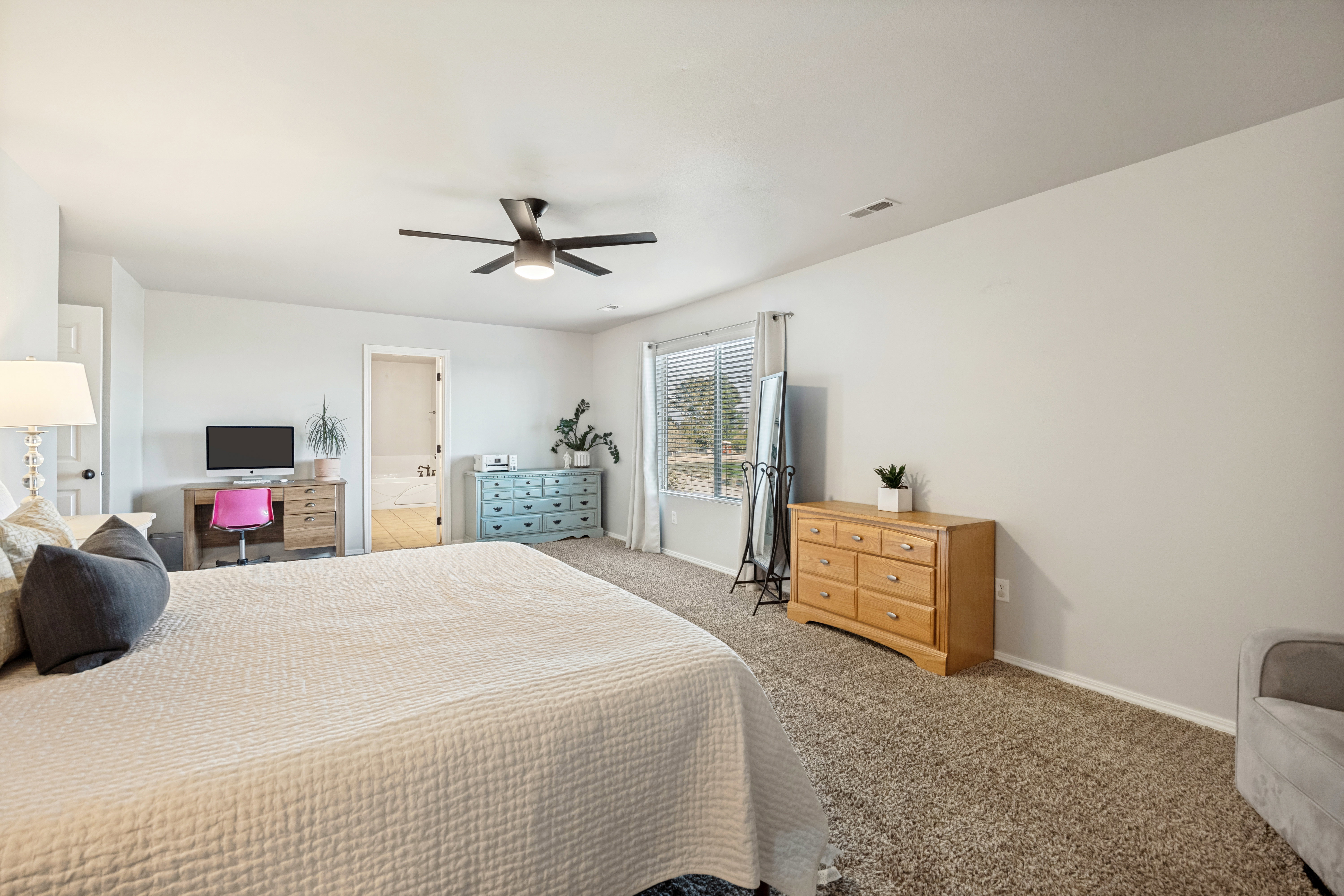 Expansive room featuring neutral wall tones, textured carpeting, a window with horizontal blinds, a ceiling fan with integrated lighting, and a white interior door
