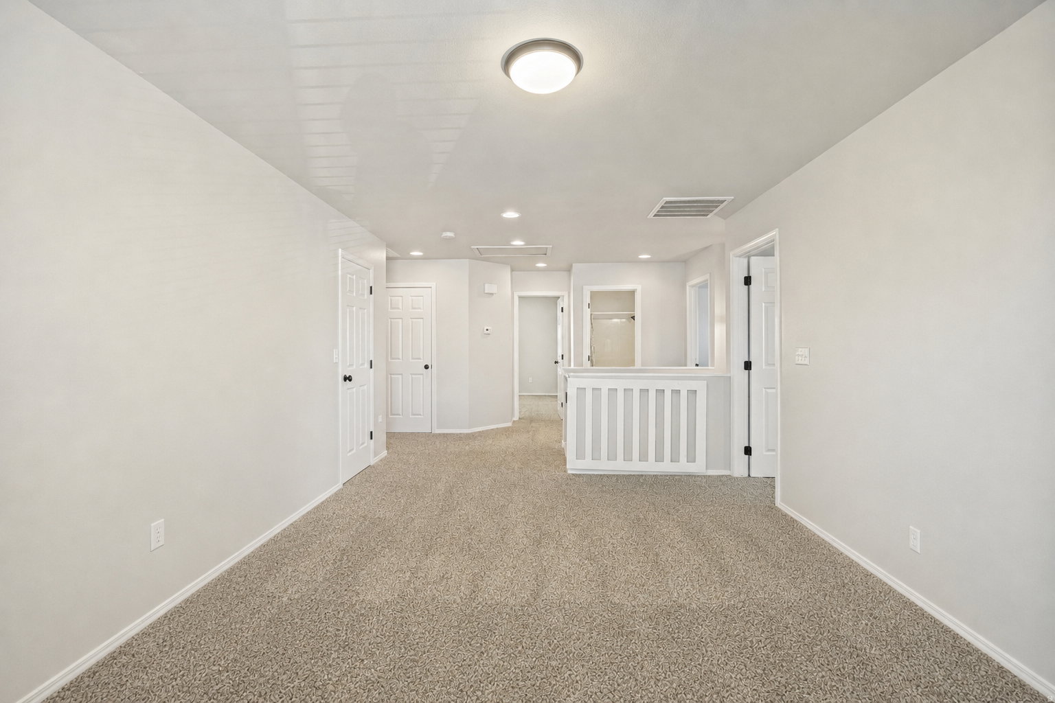 Carpeted interior space featuring light-colored walls, white trim, and multiple white doors with black hardware