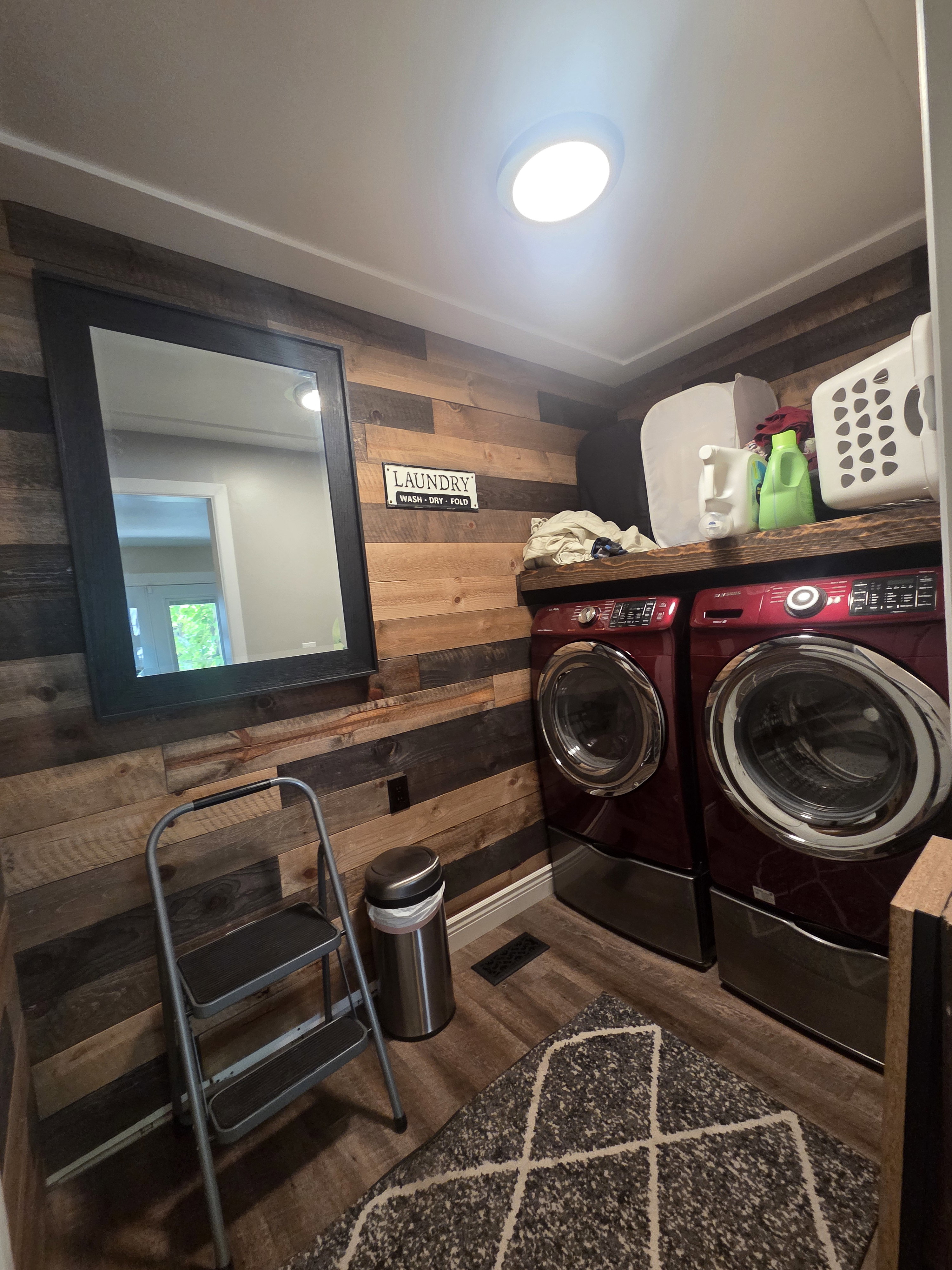 Laundry area featuring wood-panel accent wall and wood-finish flooring