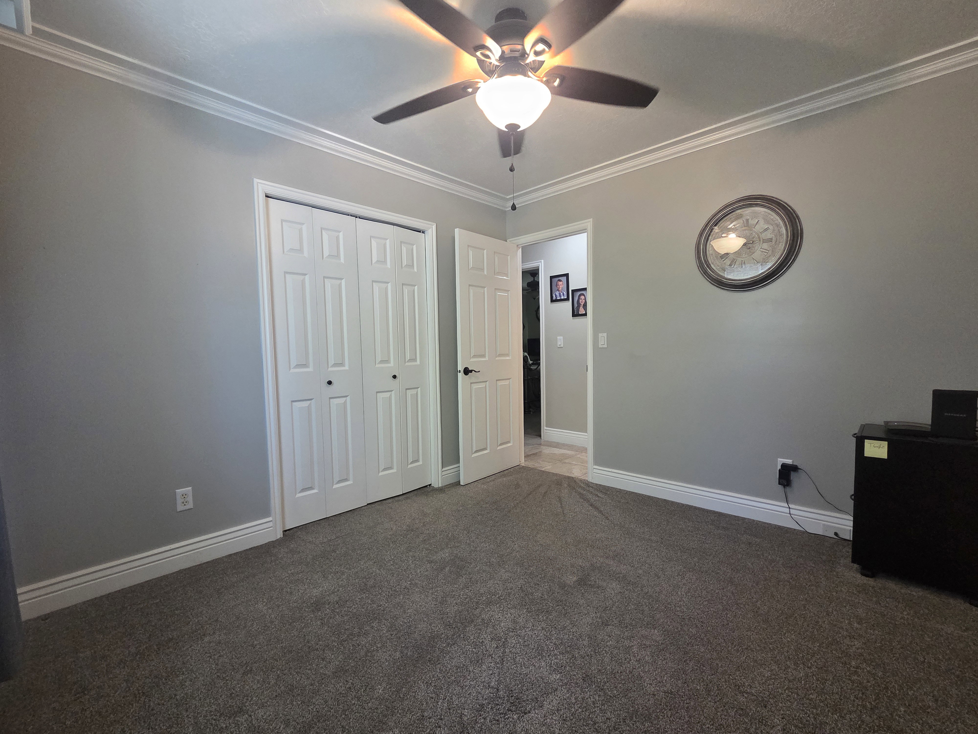Carpeted room featuring crown molding, neutral wall paint, white baseboards, a ceiling fan with light fixture, and a built-in closet with bi-fold doors