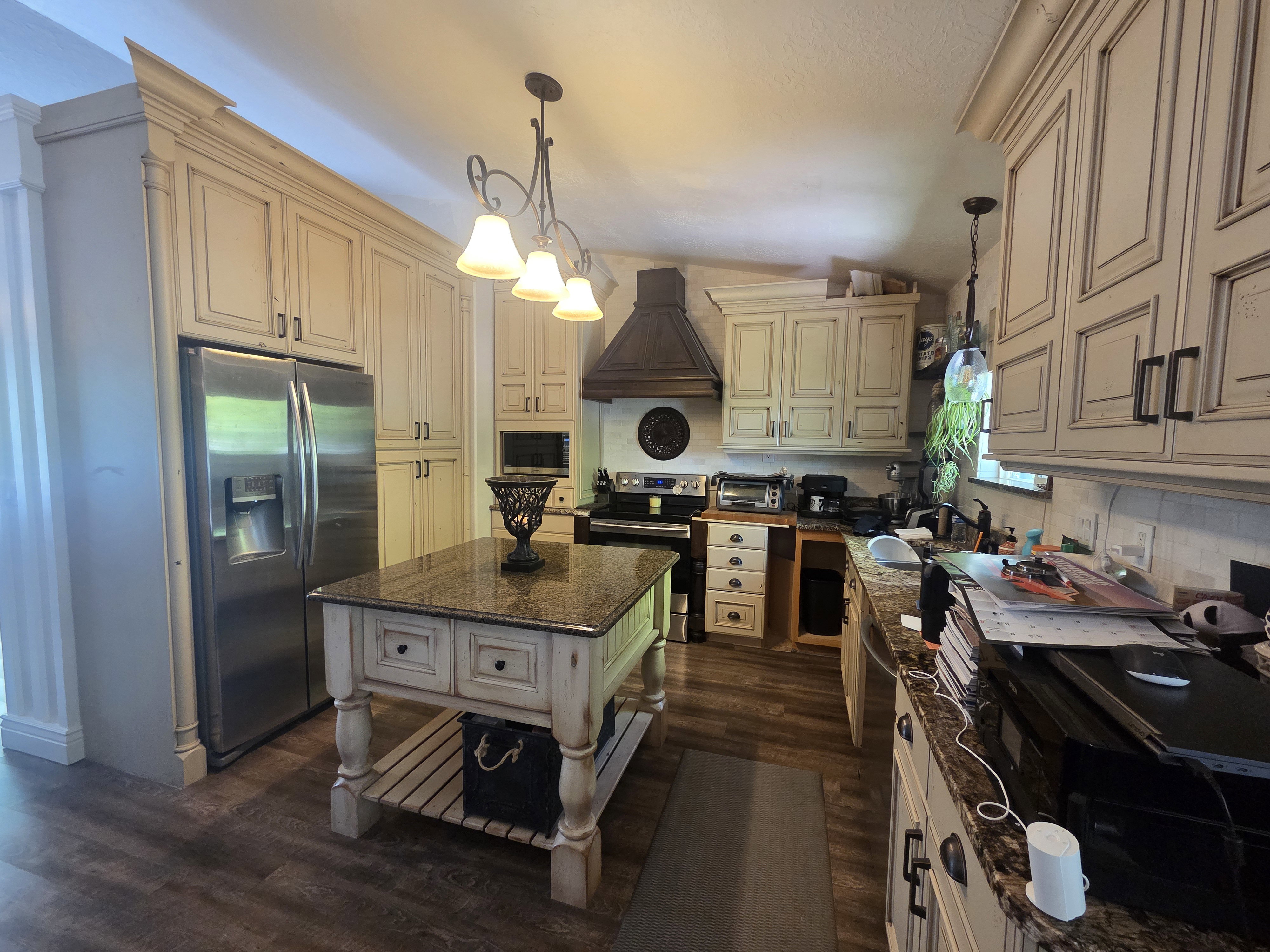Kitchen featuring extensive cream-finished cabinetry, stainless steel appliances, a freestanding island with a granite-style countertop, and wood-finish flooring