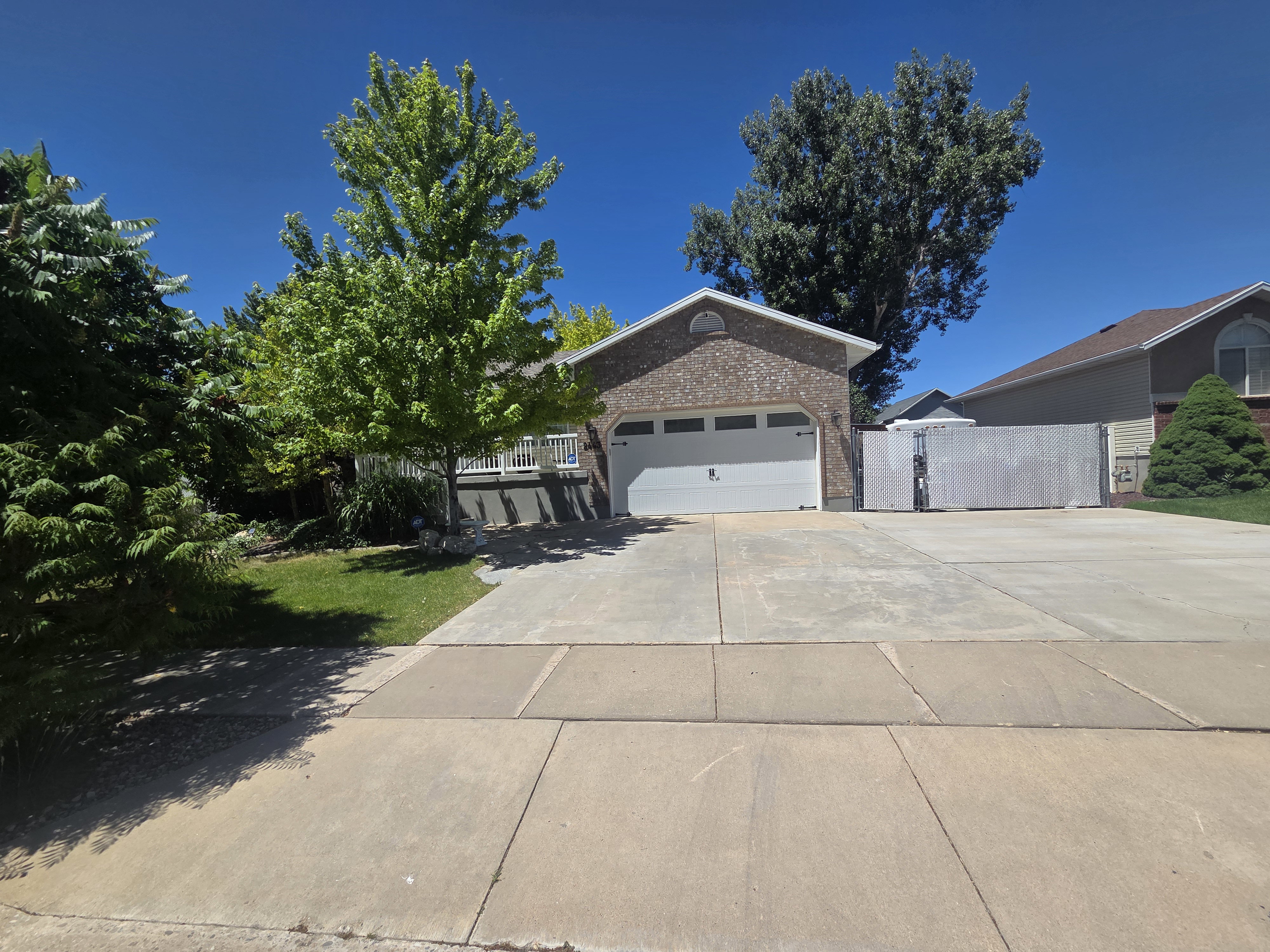 Brick-front residence featuring an attached two-car garage with a white door, a concrete driveway, and a white fence