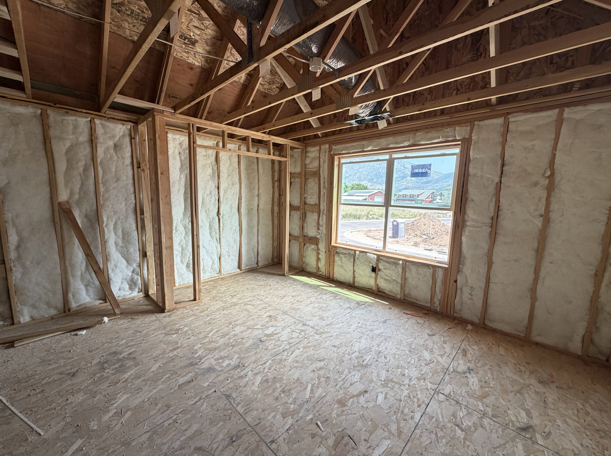 Framed interior space featuring insulated walls, an exposed beam ceiling, plywood subflooring, and a window with mountain scenery