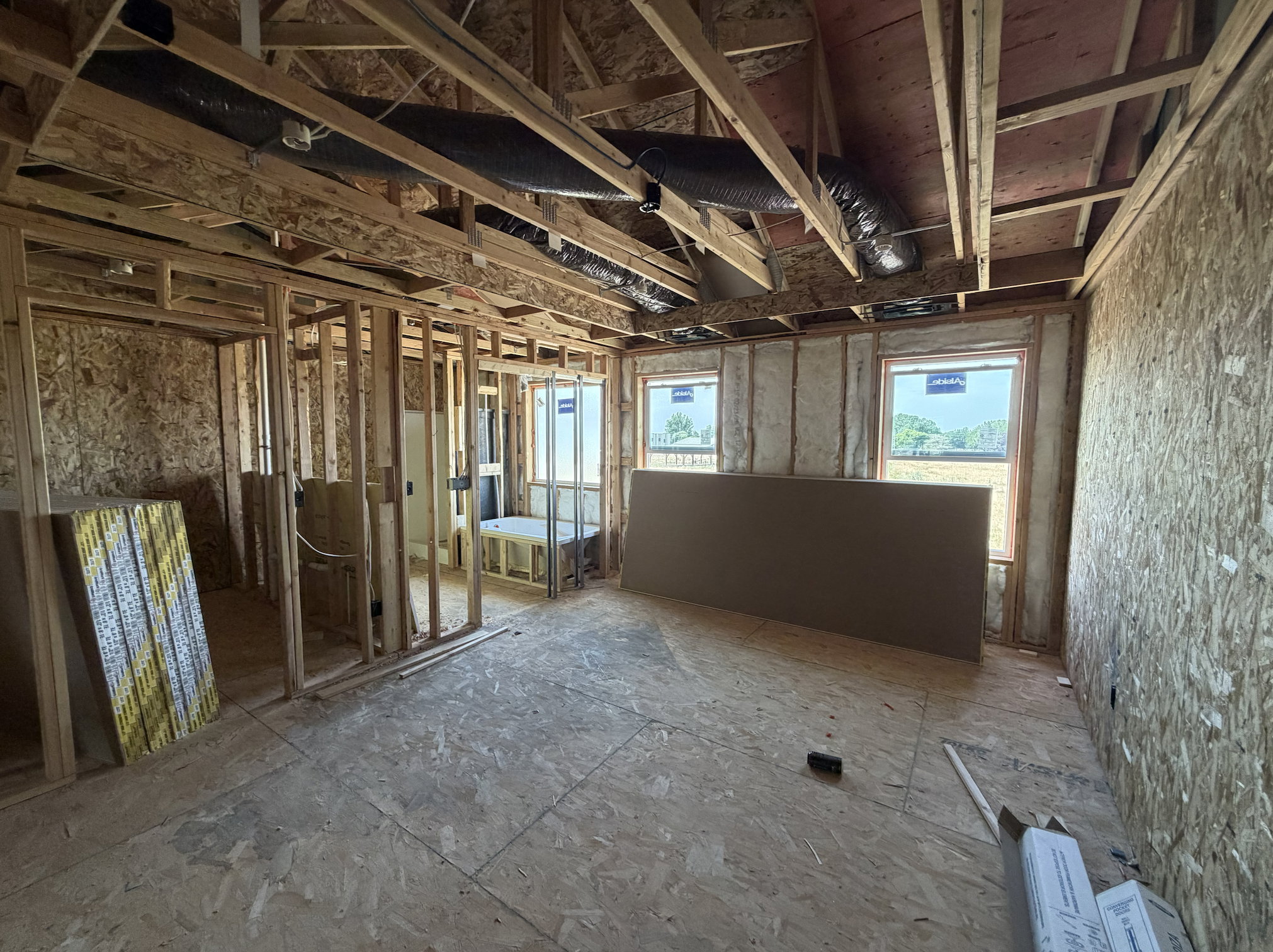 Open-concept framing with exposed ceiling joists and ductwork, multiple window openings, and a durable subfloor