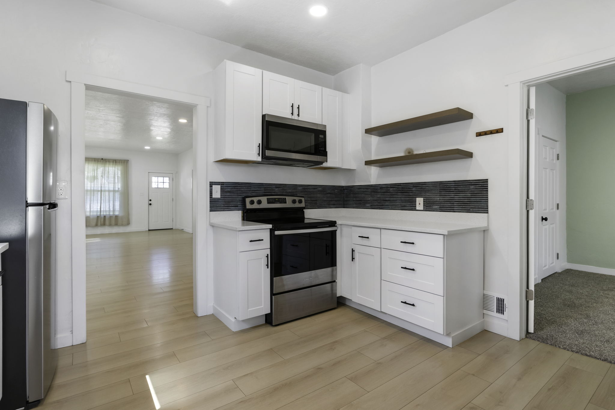 Kitchen featuring white cabinetry, stainless steel appliances, dark gray tile backsplash, light wood-finish flooring, and open shelving