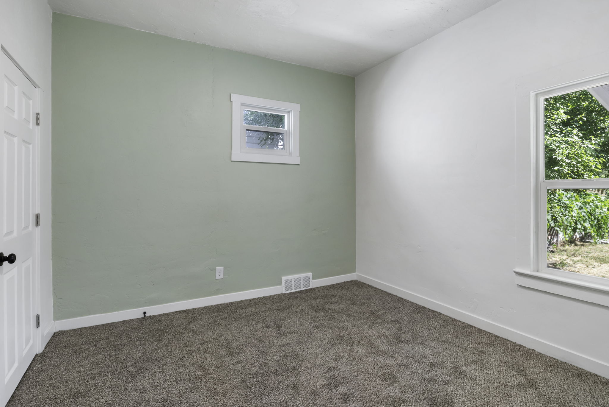 Carpeted room featuring a white door with a black knob, a single window with white trim, a second window with white trim, and a light green accent wall