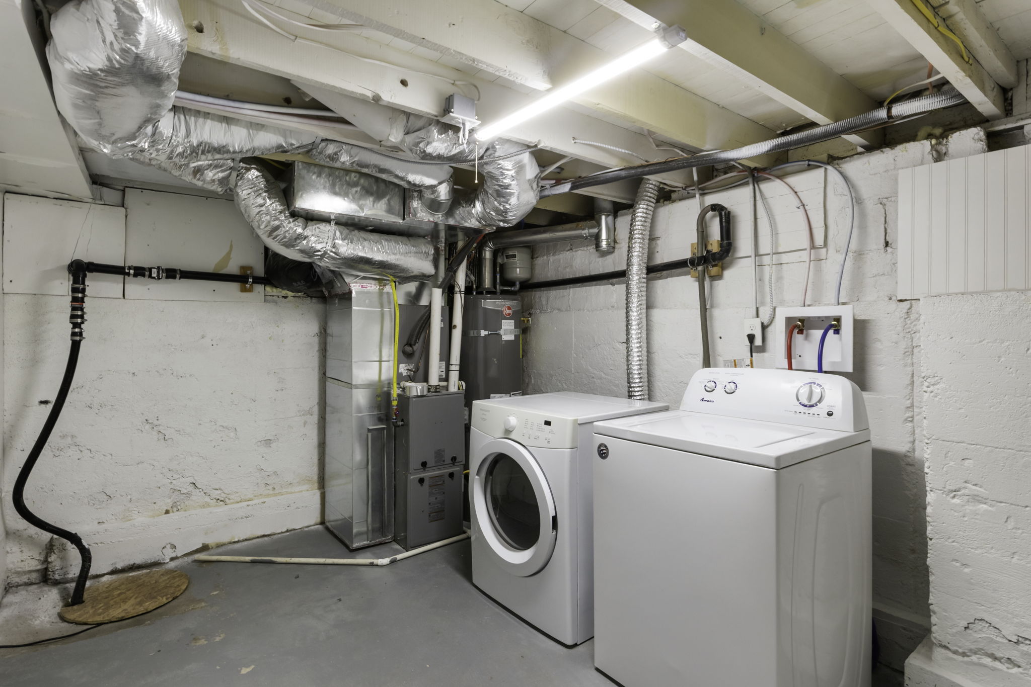 Utility area featuring exposed overhead ductwork, fluorescent lighting, and a sump pump