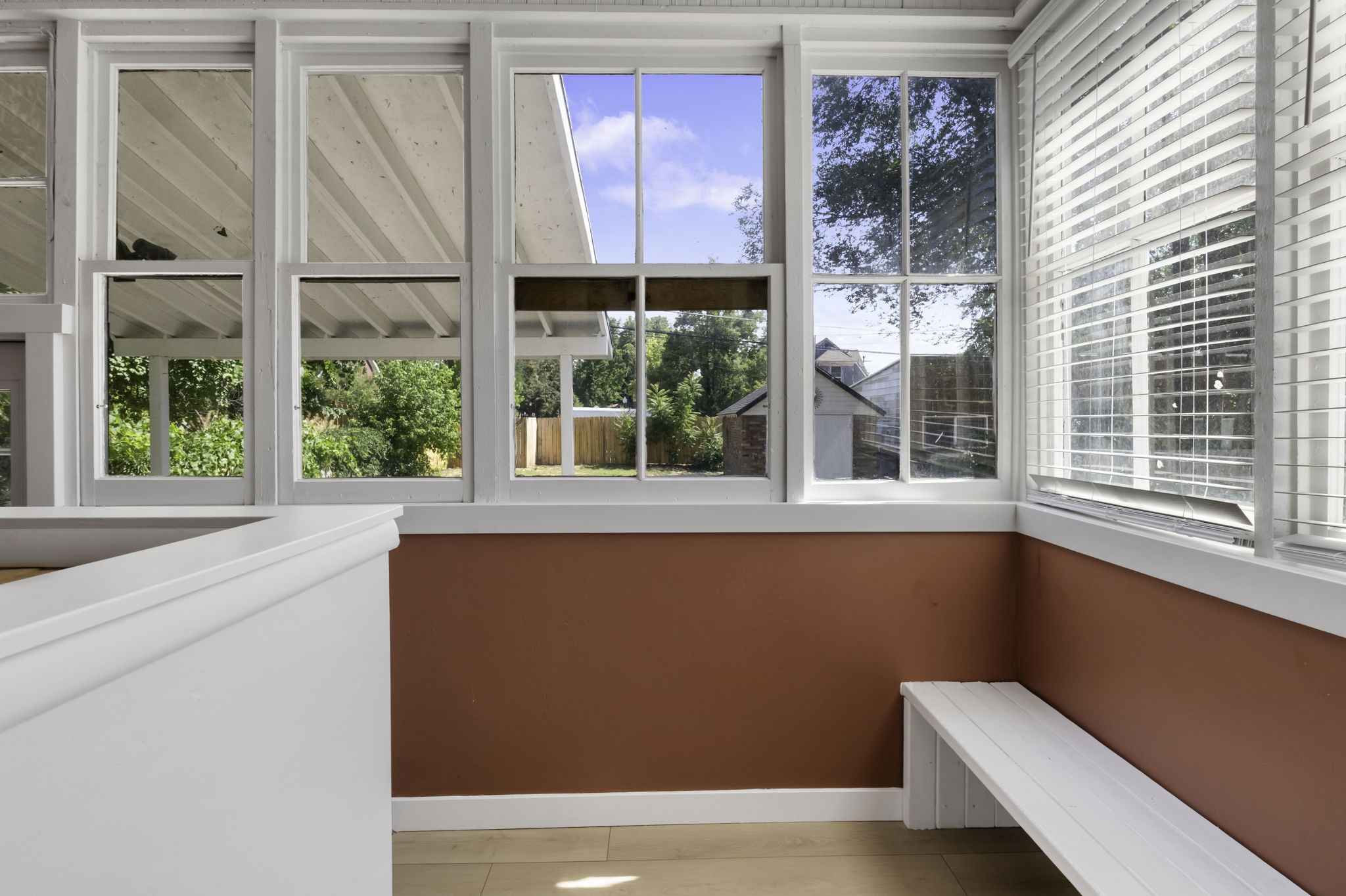 Sunroom featuring multiple vertical windows, a built-in white bench, white trim work, and wood-finish flooring