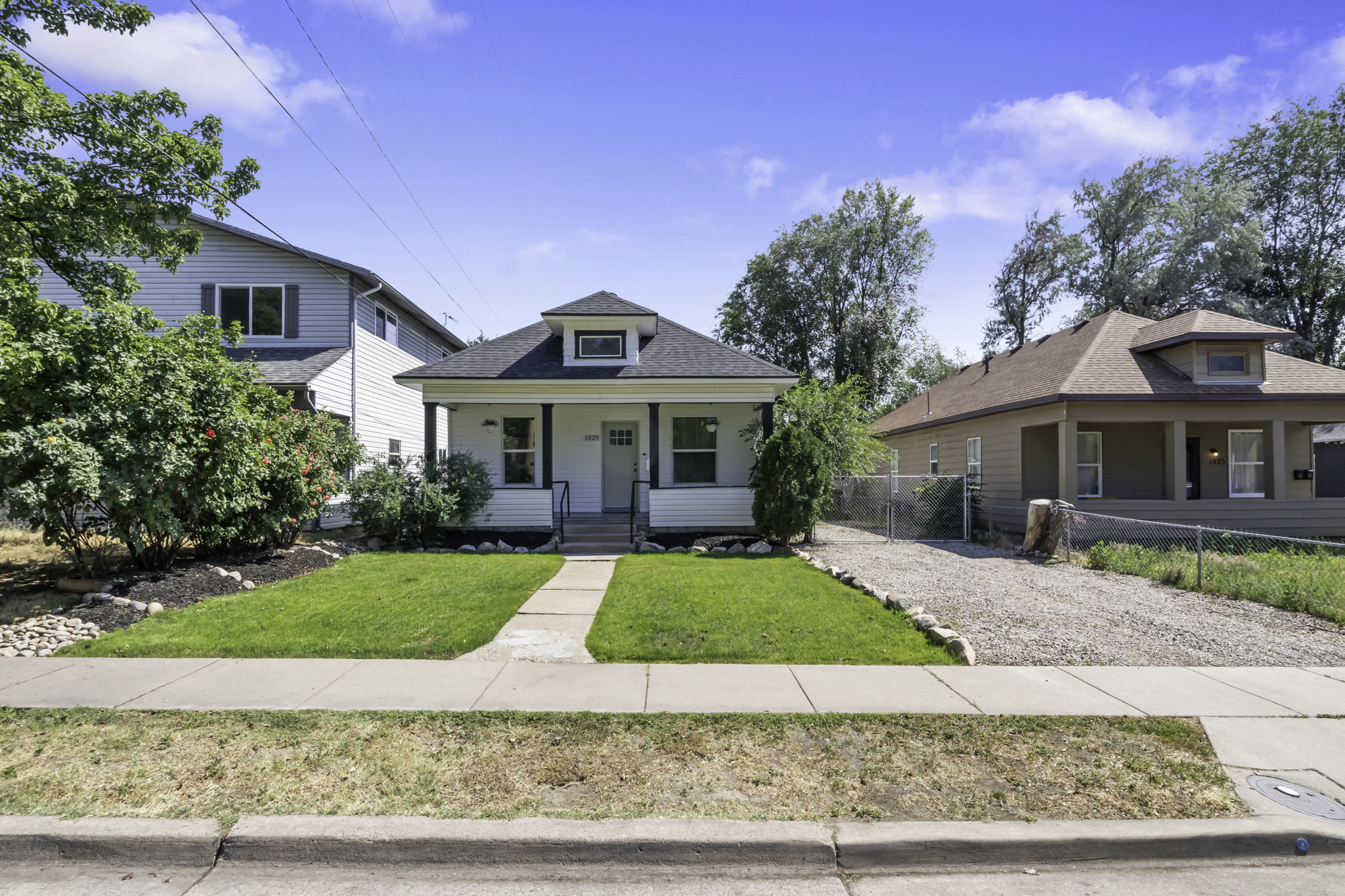Charming white siding exterior with a welcoming covered front porch, a well-maintained lawn, and a gravel driveway