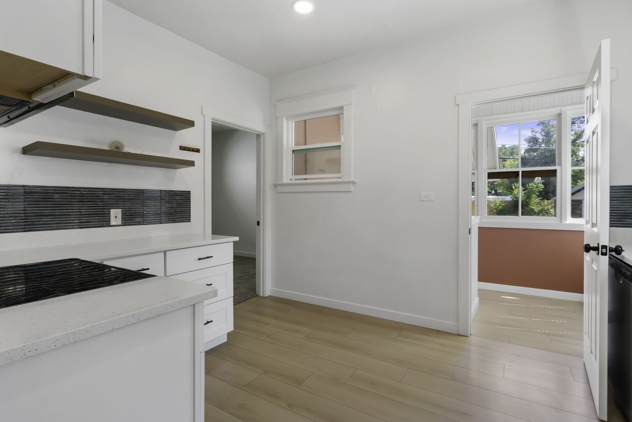Bright kitchen featuring wood-finish flooring, white cabinetry, integrated cooktop, stone countertops, and open shelving