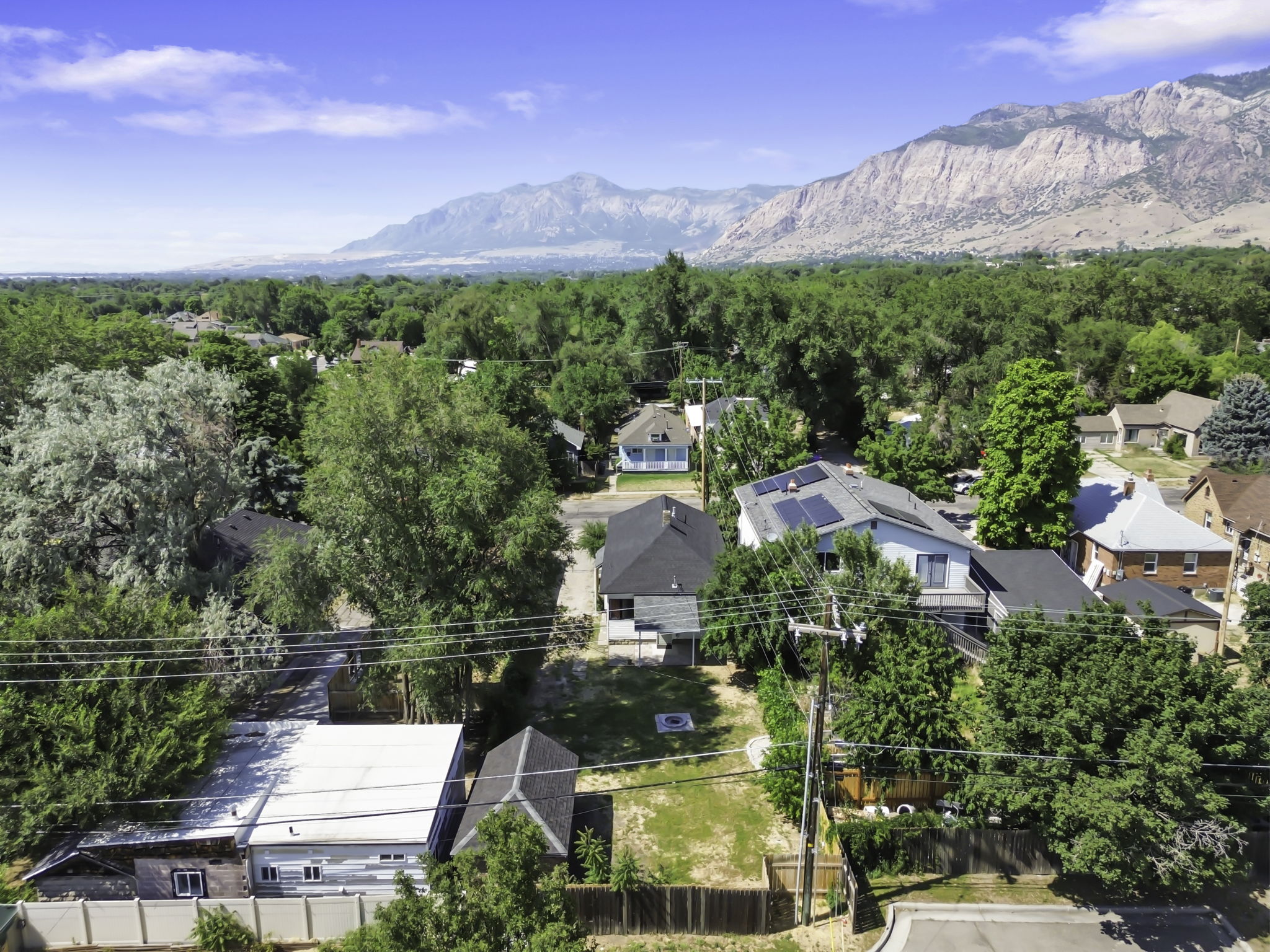 Property featuring a light-colored exterior with dark roof, multiple mature trees, and a mountain backdrop