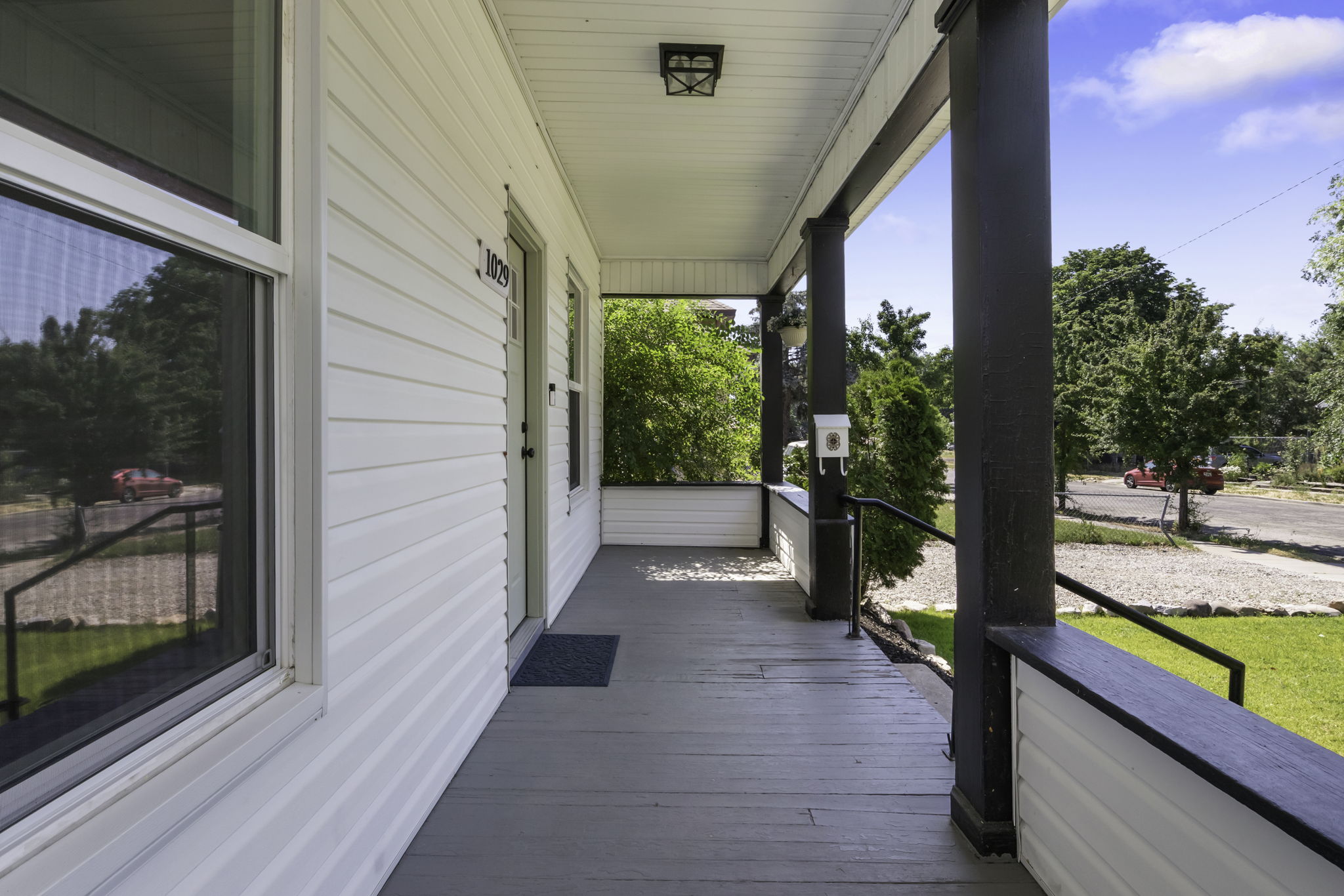 Covered front porch featuring white siding, dark support columns, black railings, and a contrasting gray floor