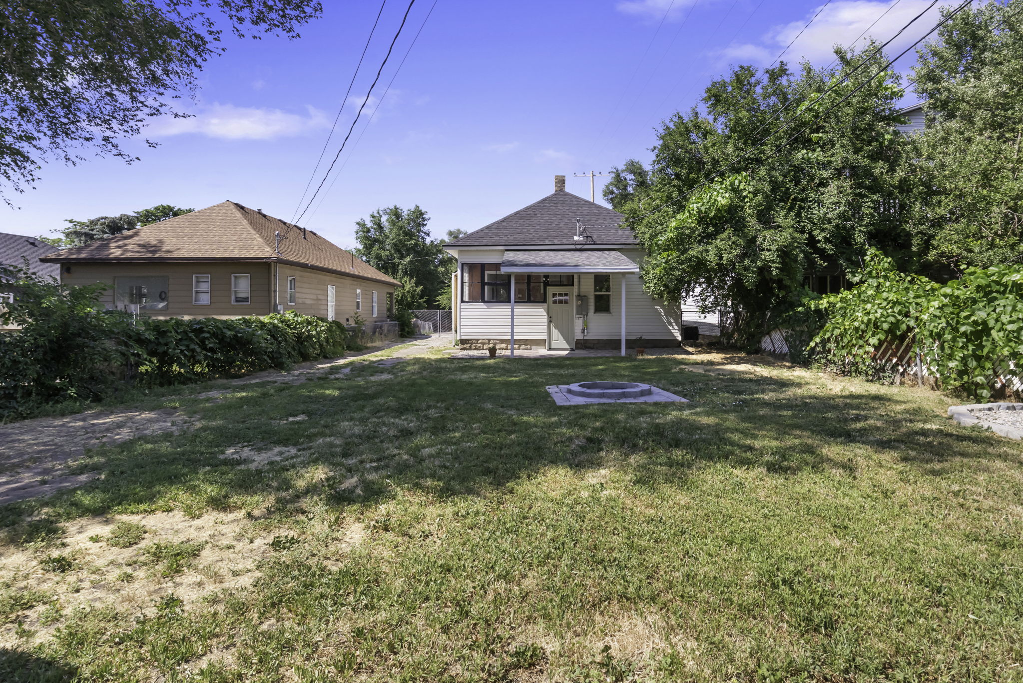 Spacious backyard featuring a built-in fire pit, mature trees, and a covered porch entry