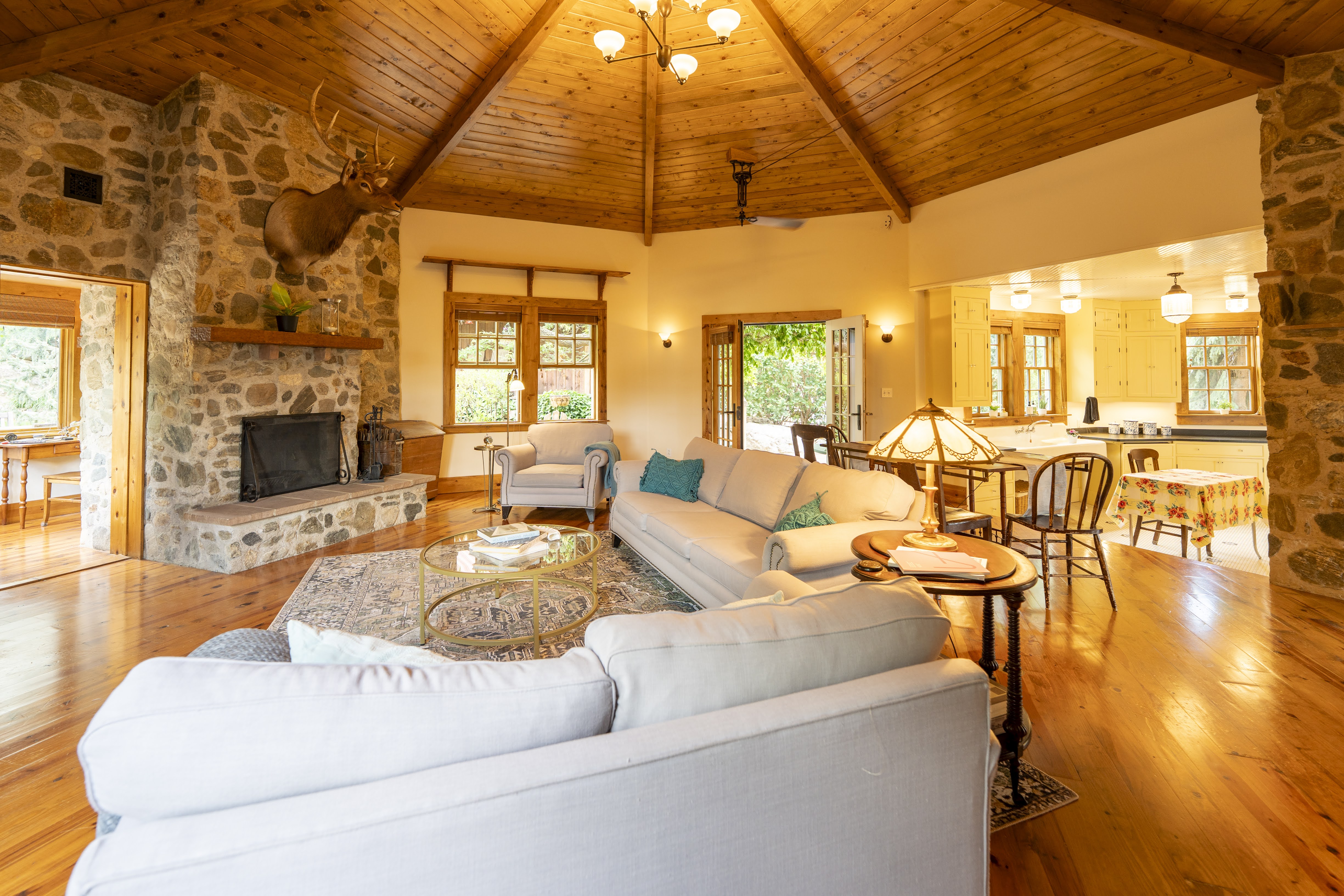 Spacious living area featuring a stone-clad fireplace with a wood mantel, exposed wood-beam vaulted ceiling, and polished wood-finish flooring