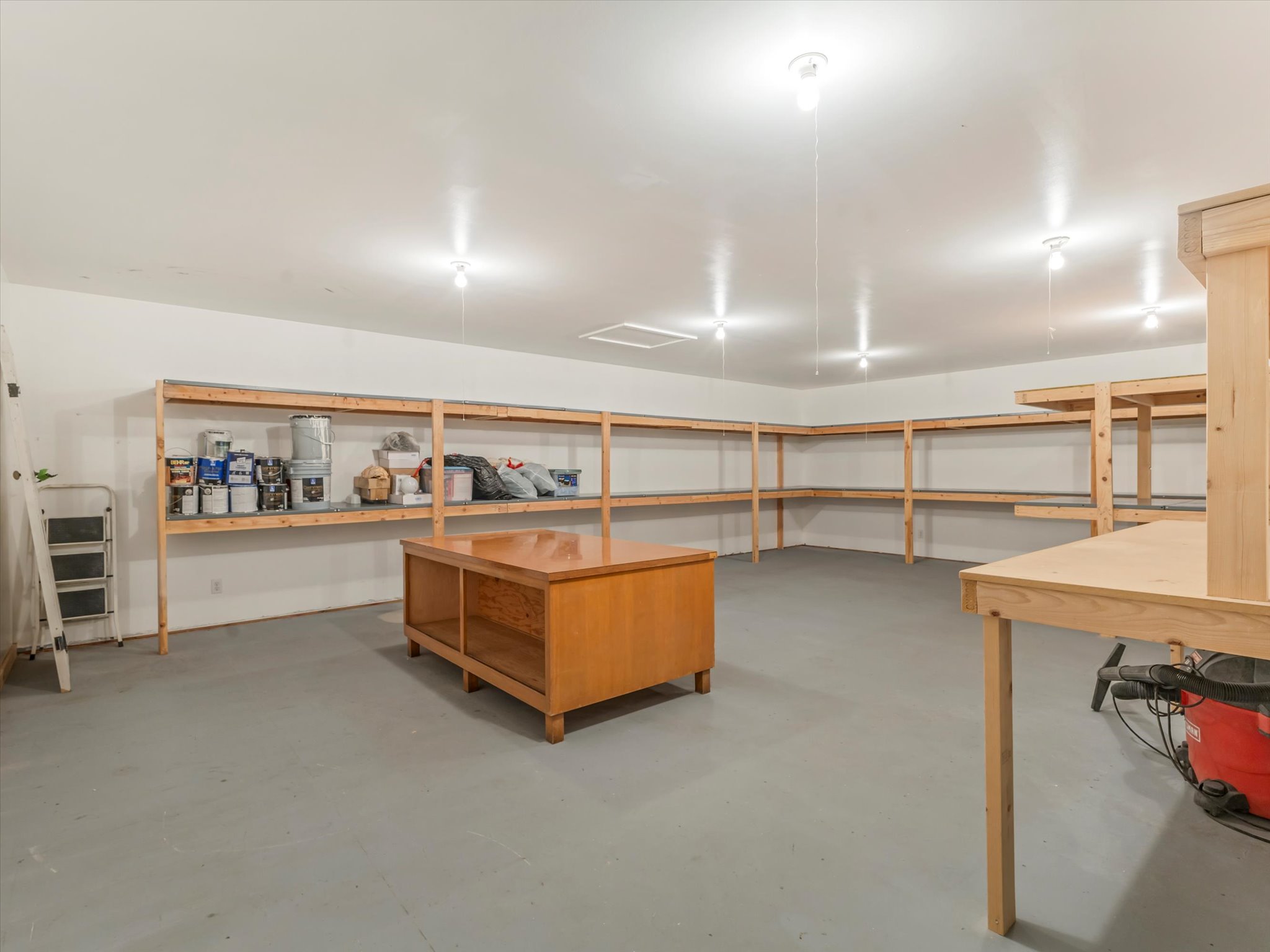 ADU Spacious utility room featuring extensive built-in wooden shelving, a painted concrete floor, and multiple ceiling-mounted light fixtures