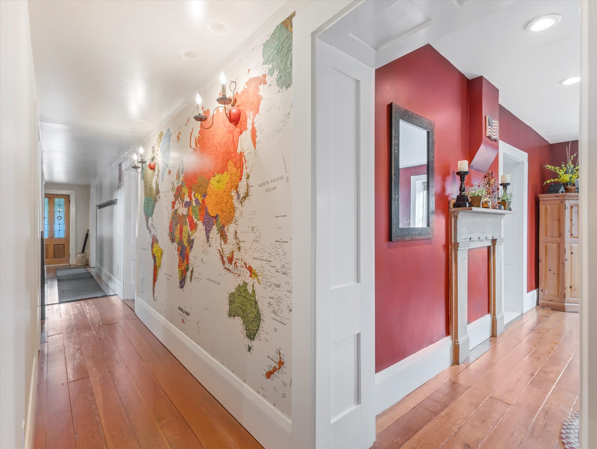 Hallway featuring wood-finish flooring, a decorative wall map, wall-mounted sconces, and a painted red wall