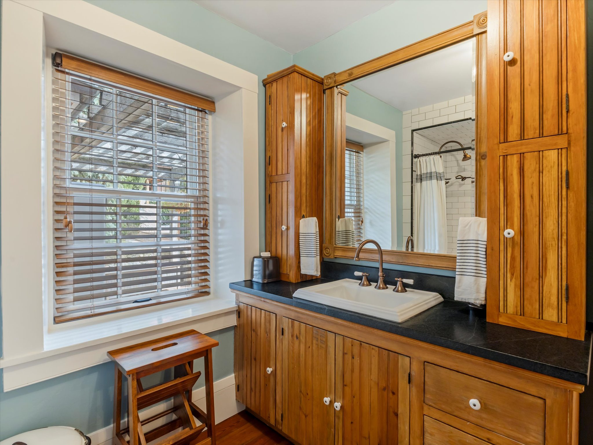 Bathroom featuring a wood-finish vanity with an integrated sink, dark countertop, and a large framed mirror