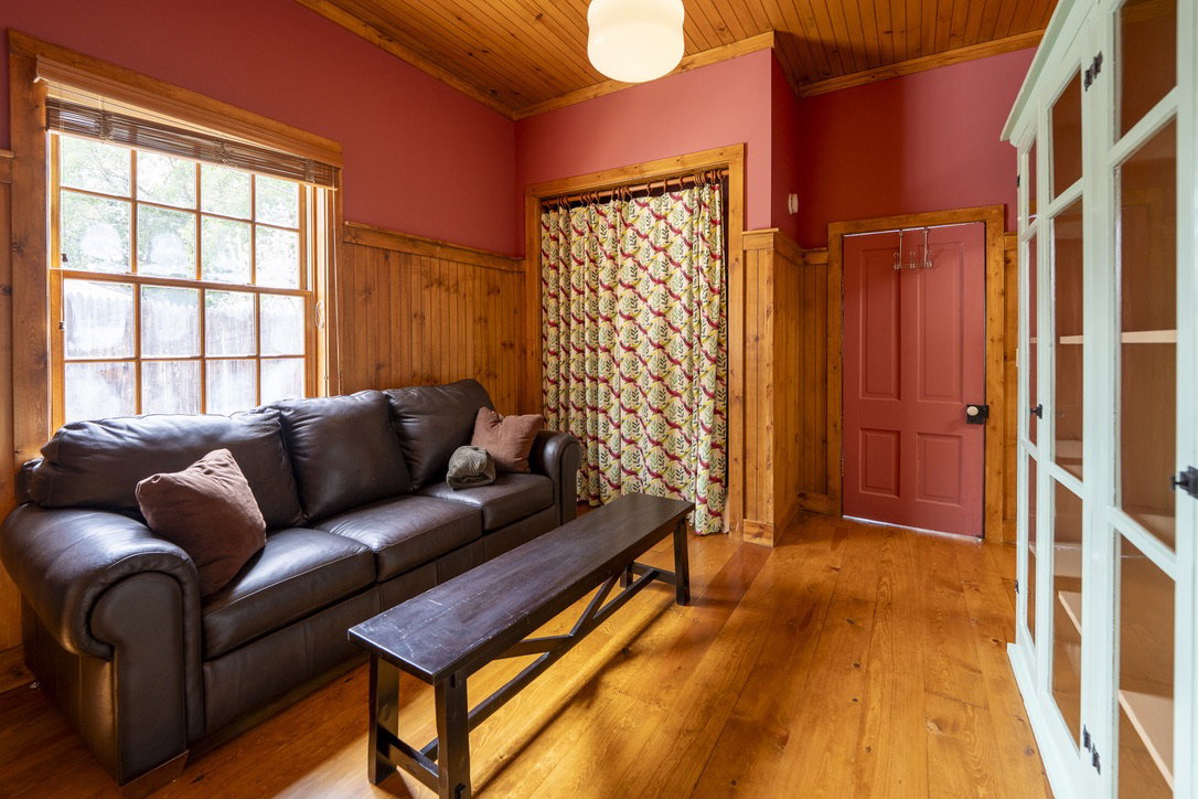 Guest bedroom in ADU. Hardwood flooring throughout featuring wood paneling on lower walls, a wood-finish ceiling, and a multi-pane window with a wood frame
