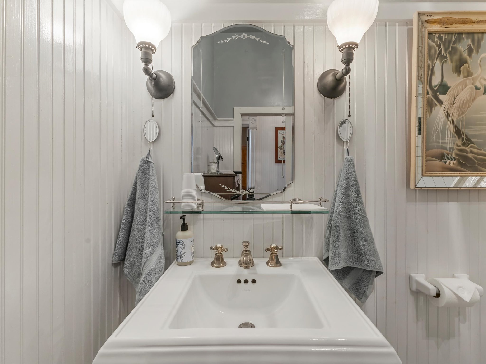 Pedestal sink featuring brass-finish fixtures, a glass shelf, and a framed mirror
