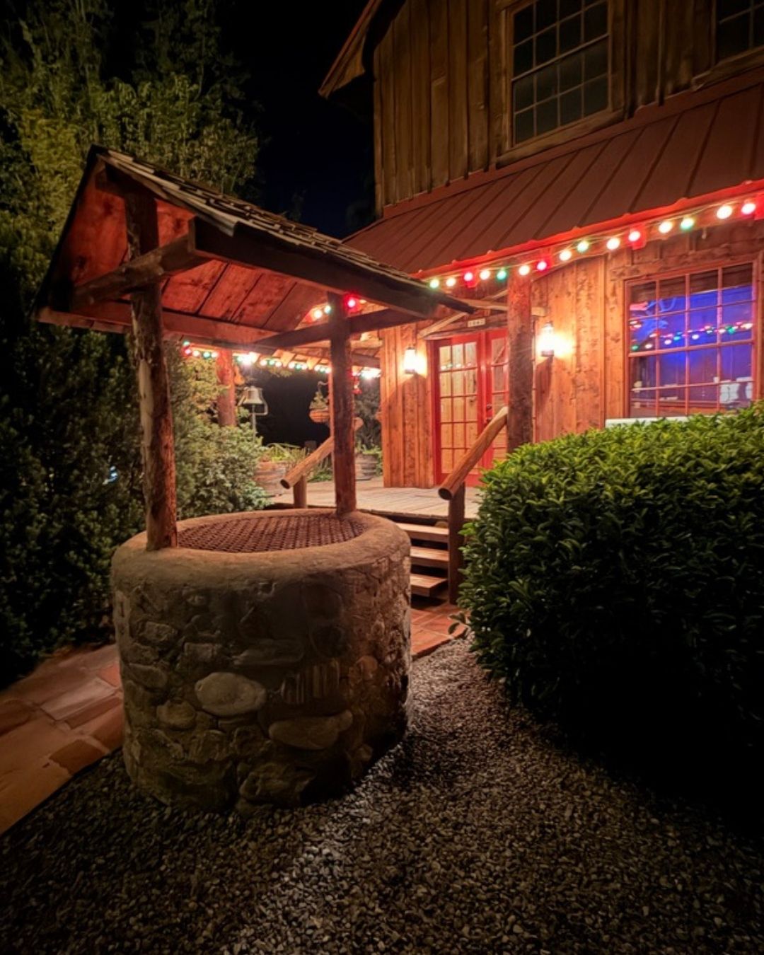 Stone-clad well feature with a wood shingle roof, positioned on a gravel bed