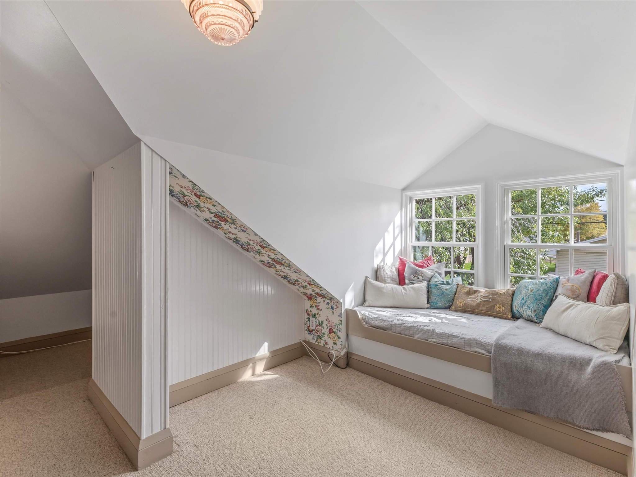 Attic space featuring a built-in window seat, two large windows, vaulted ceilings, and carpeted flooring