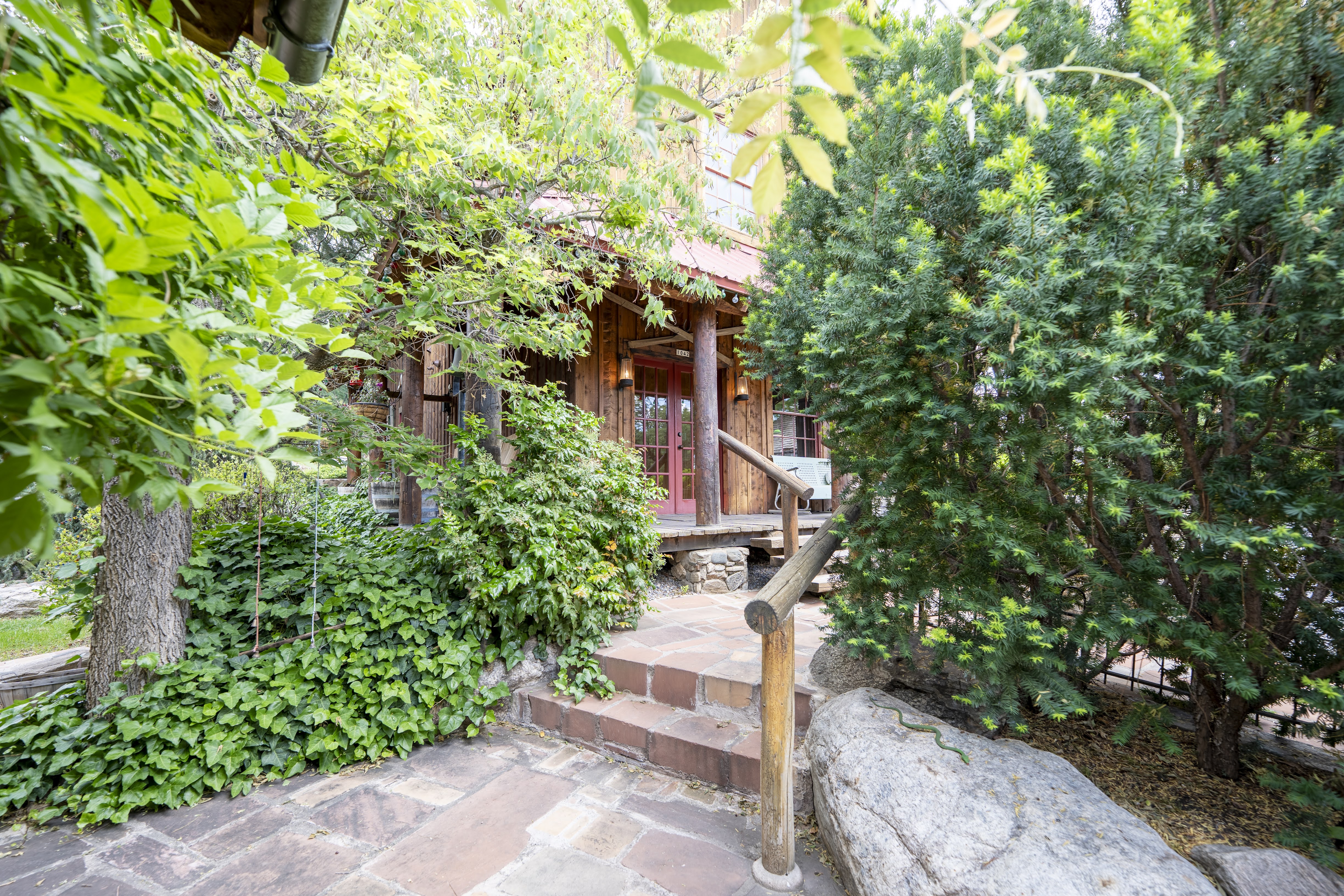 Exterior featuring wood siding, a covered porch with round wood columns, and a terraced stone and brick pathway