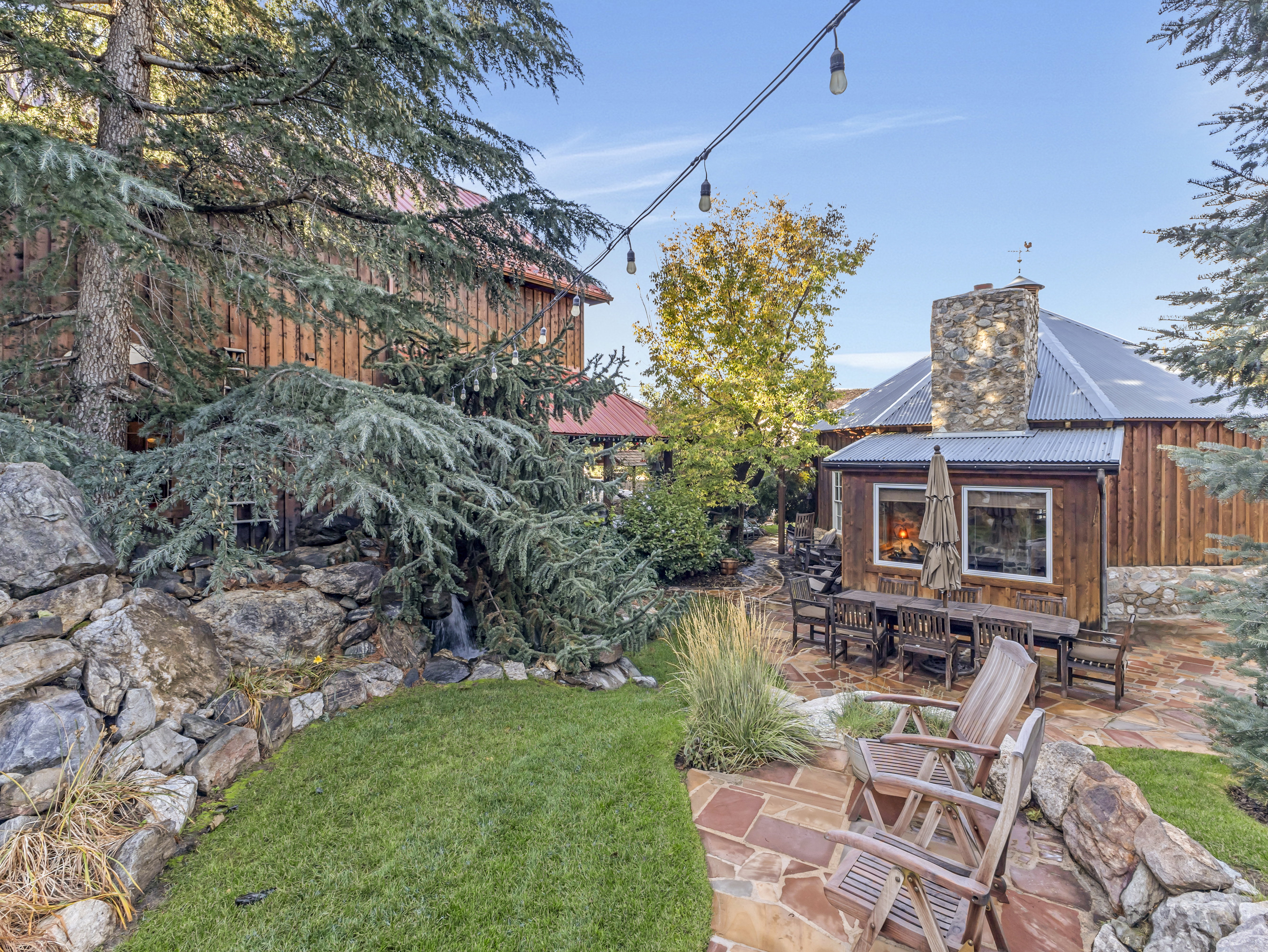 Outdoor living space featuring a flagstone patio, manicured lawn, and a natural rock wall with a water feature
