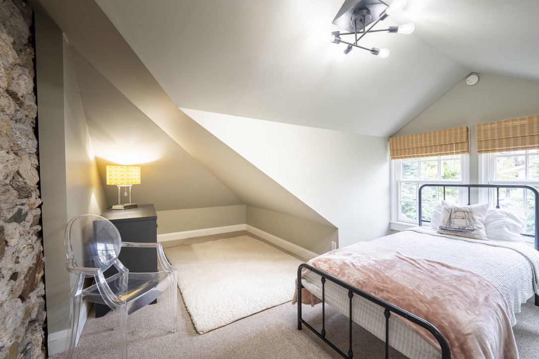 Bedroom featuring sloped ceilings, a prominent stone accent wall, and carpet flooring