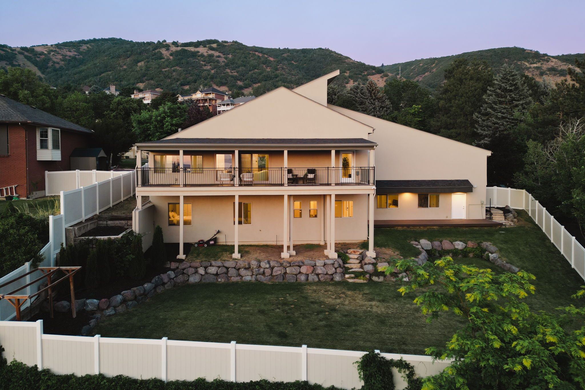 Rear exterior featuring a full-width upper-level balcony with metal railings, a lower-level walk-out patio, a sloped lawn, and a privacy fence